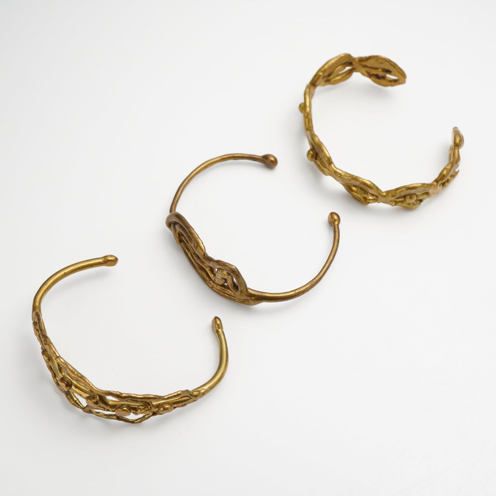 Three Sonia Rykiel Modernist Copper Cuff Bracelets: This lot features three copper cuff bracelets by Sonia Rykiel, each exhibiting a modernist, brutalist aesthetic with an organic, matte gold-tone finish. The first bracelet is a continuous wide band fe