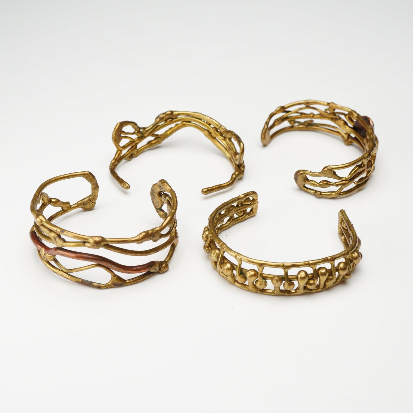 4pc Brass Modernist Studio Jewelry Cuff Bracelets: This collection includes 4pc brass cuff bracelets featuring a hand-crafted, organic aesthetic characteristic of the mid-20th-century Brutalist movement. The group contains a multi-strand cuff with int