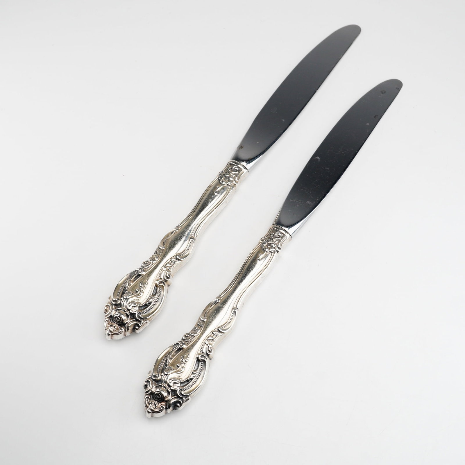 2pc Gorham Sterling Silver and Stainless Steel Dinner Knives, La Scala: A pair of dinner knives manufactured by Gorham in the La Scala pattern. The handles are constructed of sterling silver and feature a highly ornate Rococo-revival design with elaborate scrollwork, flor