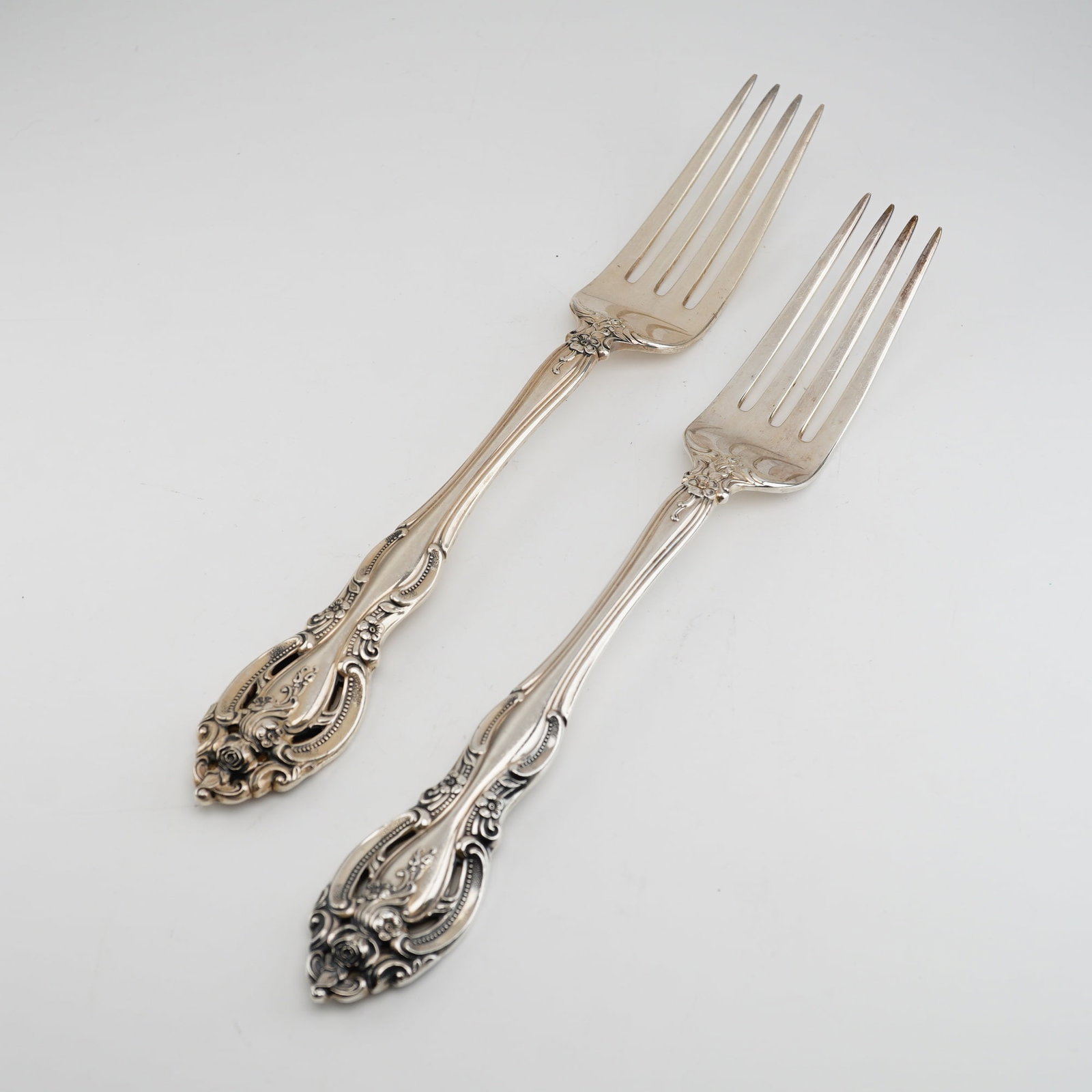2pc Gorham Sterling Silver Dinner Forks, La Scala: The design reflects the Rococo Revival style, featuring ornate scrolled borders, shell motifs, and floral accents, most notably a rose located at the terminal of the handle. The reverse side of each f