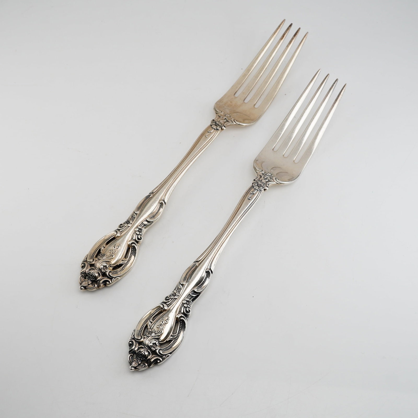 2pc Gorham Sterling Silver Dinner Forks, La Scala: High-relief floral motifs including roses and buttercups, framed by scrollwork and a shaped, pierced-look terminal. The reverse of each handle is stamped with the maker marks consisting of a lion pass