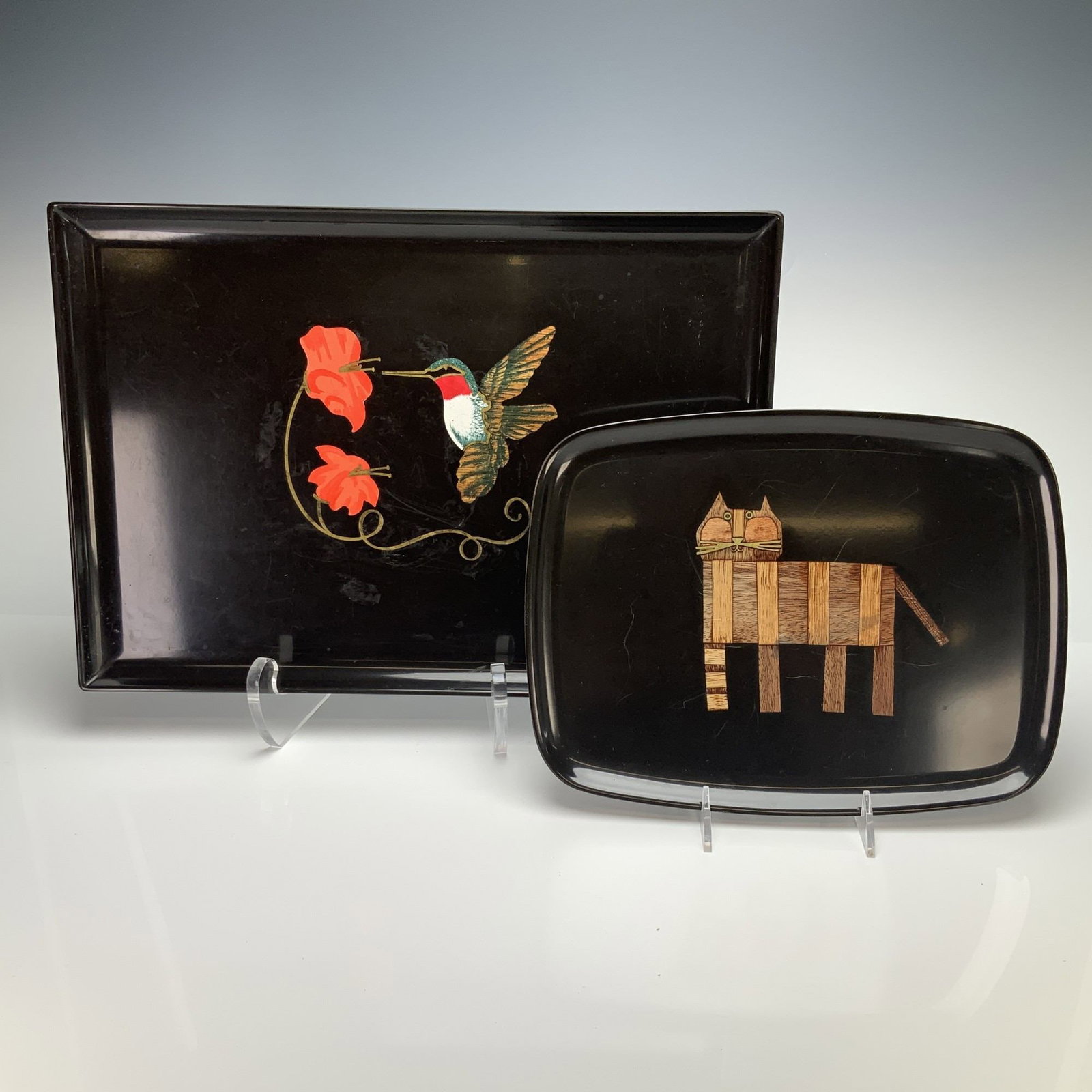 2pc Couroc of Monterey Black Lacquer Trays with Hand Inlaid Designs: A grouping of mid-century modern black lacquer serving trays by Couroc of Monterey, featuring hand inlaid designs. The larger rectangular tray depicts a hummingbird in flight approaching two orange fl
