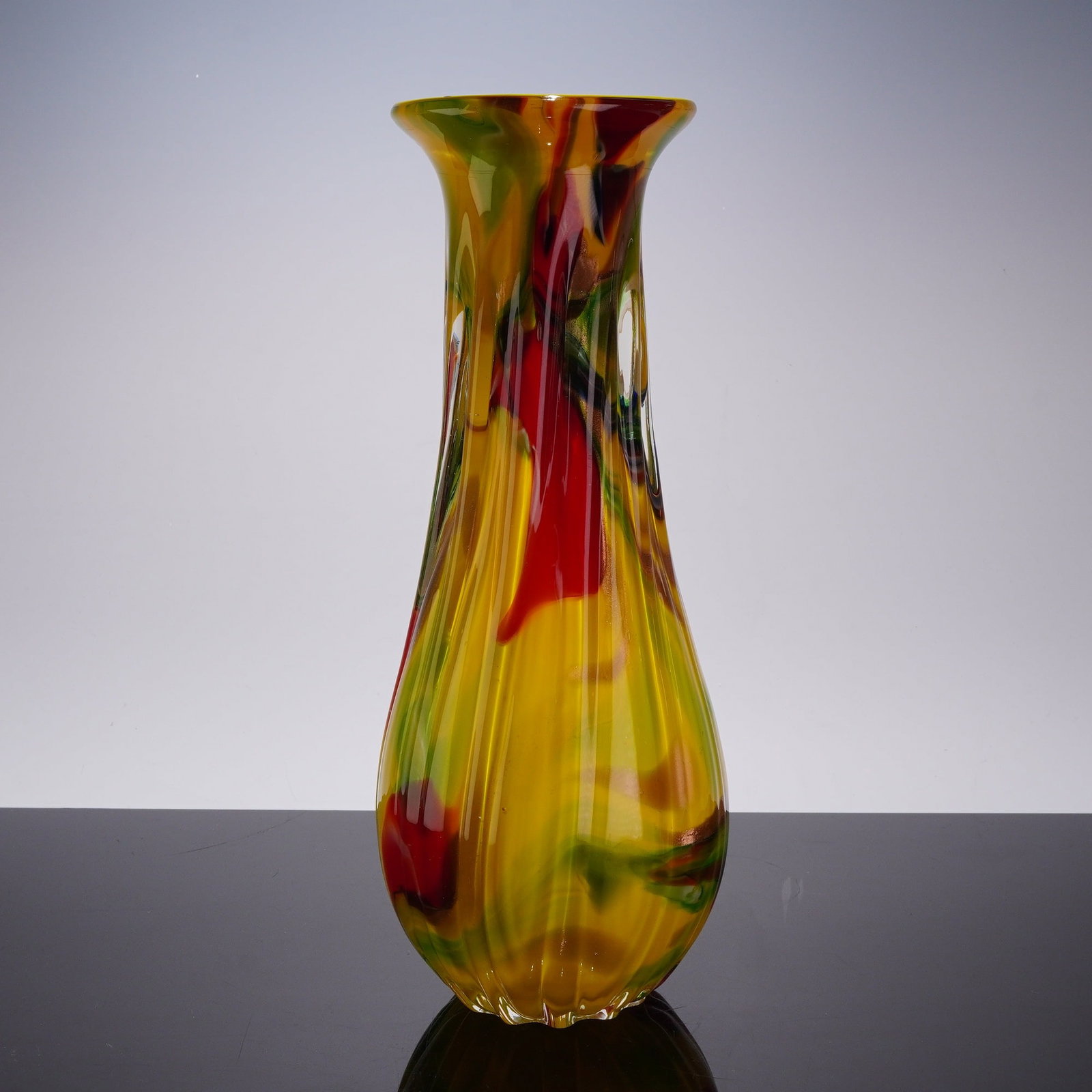 Hand-Blown Yellow Art Glass Vase with Multi-Colored Decoration and Optic Ribbing: This hand-blown art glass vase features internal yellow glass with multi-colored decoration and a clear ribbed external. The vessel is designed with a flared rim, a long neck, and a bulbous base. The 