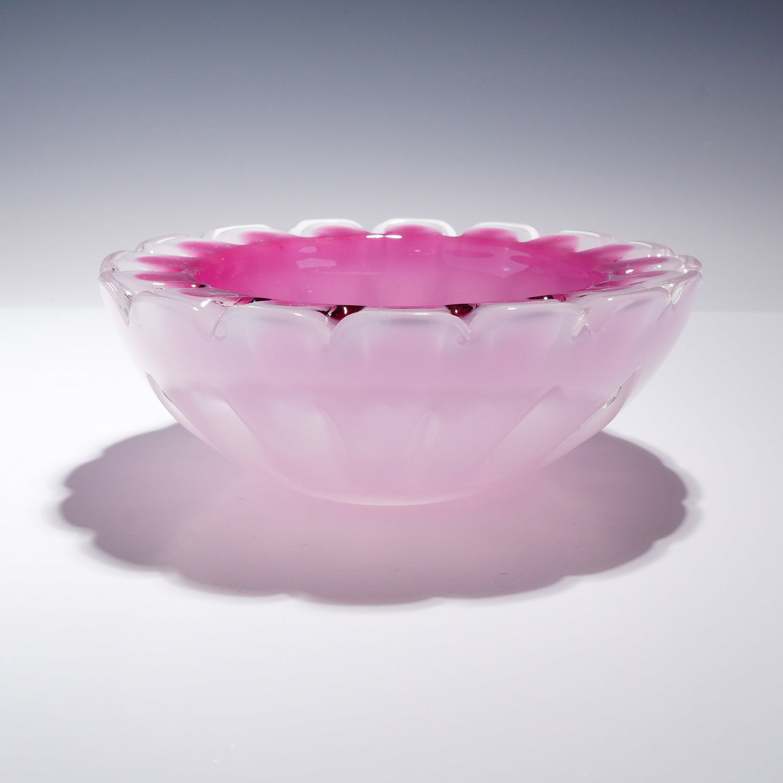 Mid-Century Modern Heavy Pink and Clear Cased Art Glass Petal Bowl: This heavy art glass bowl features a circular, shallow form with a distinctive scalloped petal rim. The piece is constructed using a casing technique, displaying a deep magenta or cranberry-toned inte