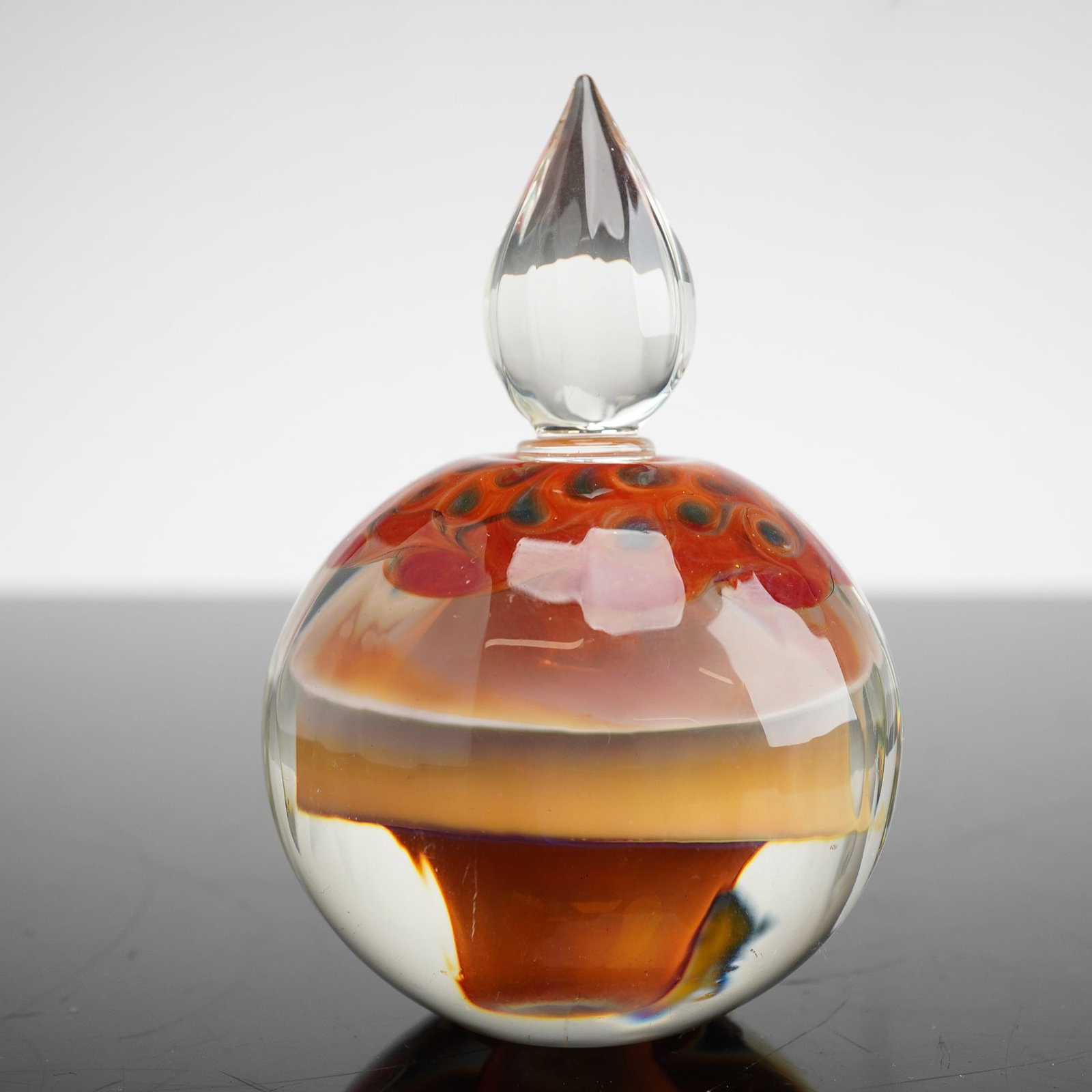 Richard Clements Studio Art Glass Scent Bottle and Stopper: A Richard Clements studio art glass scent bottle with a matching stopper. This heavy, spherical vessel is constructed of blown glass using internal layering techniques. The clear glass exterior encase