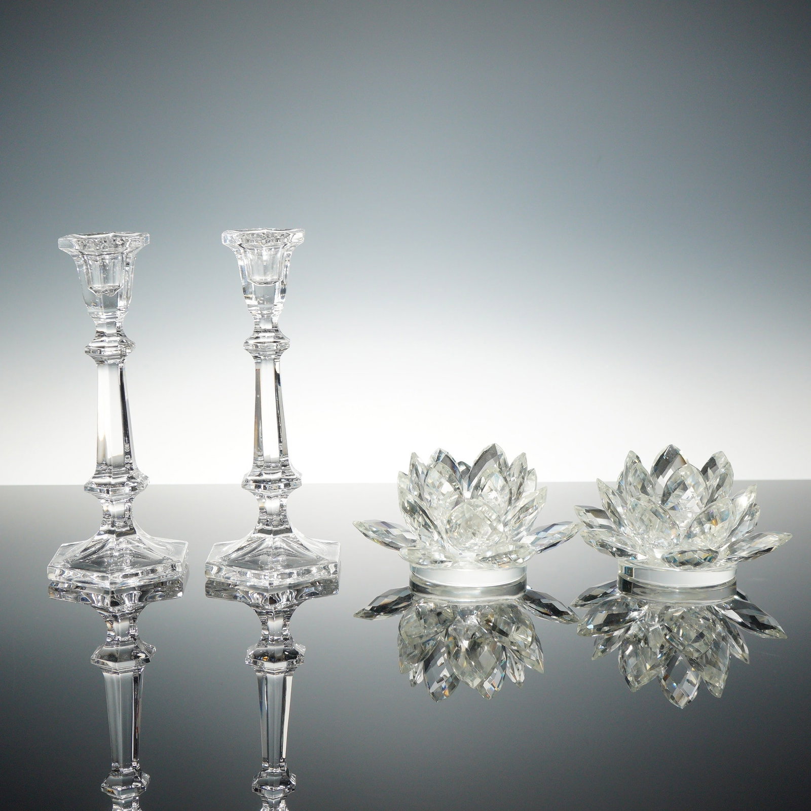 A Set of 4 Crystal Candleholders: This set of 4 crystal candleholders consists of two columnar taper candlesticks and two votive holders fashioned as blossoming lotus flowers. Each piece is crafted from clear lead crystal featuring pr