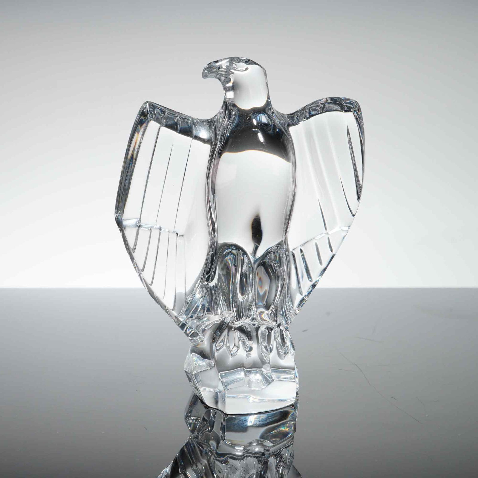Baccarat Crystal Imperator Eagle Figurine: A clear lead crystal sculpture of a baccarat eagle, specifically the Imperator model. The bird is depicted with outspread wings and is perched on a textured, rock-form base. The sculpture uses a combi