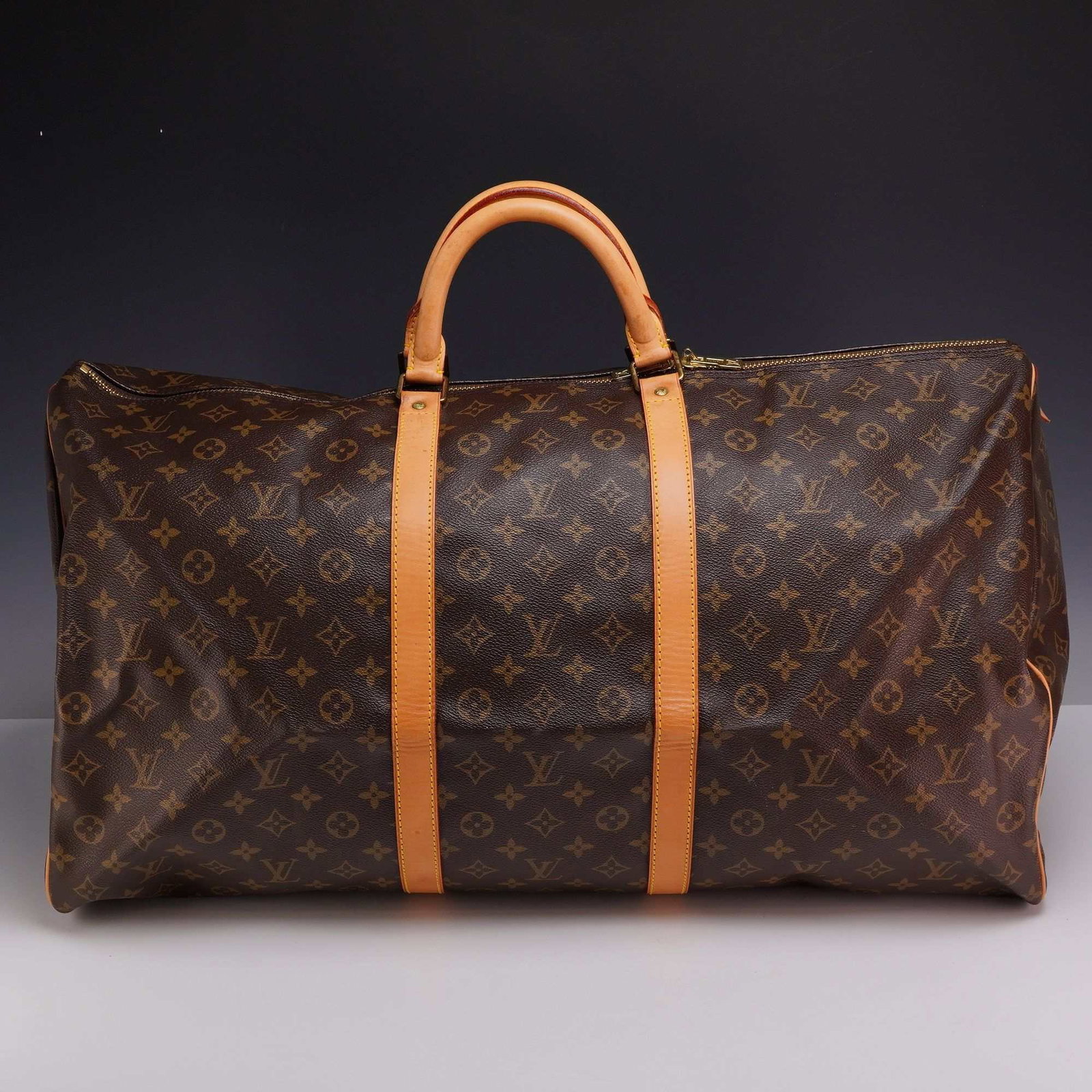Louis Vuitton Monogram Canvas Keepall Travel Bag: A Louis Vuitton large duffle travel bag in the Keepall style, featuring the iconic monogram coated canvas exterior. The bag is trimmed with natural vachetta cowhide leather, including two parallel str
