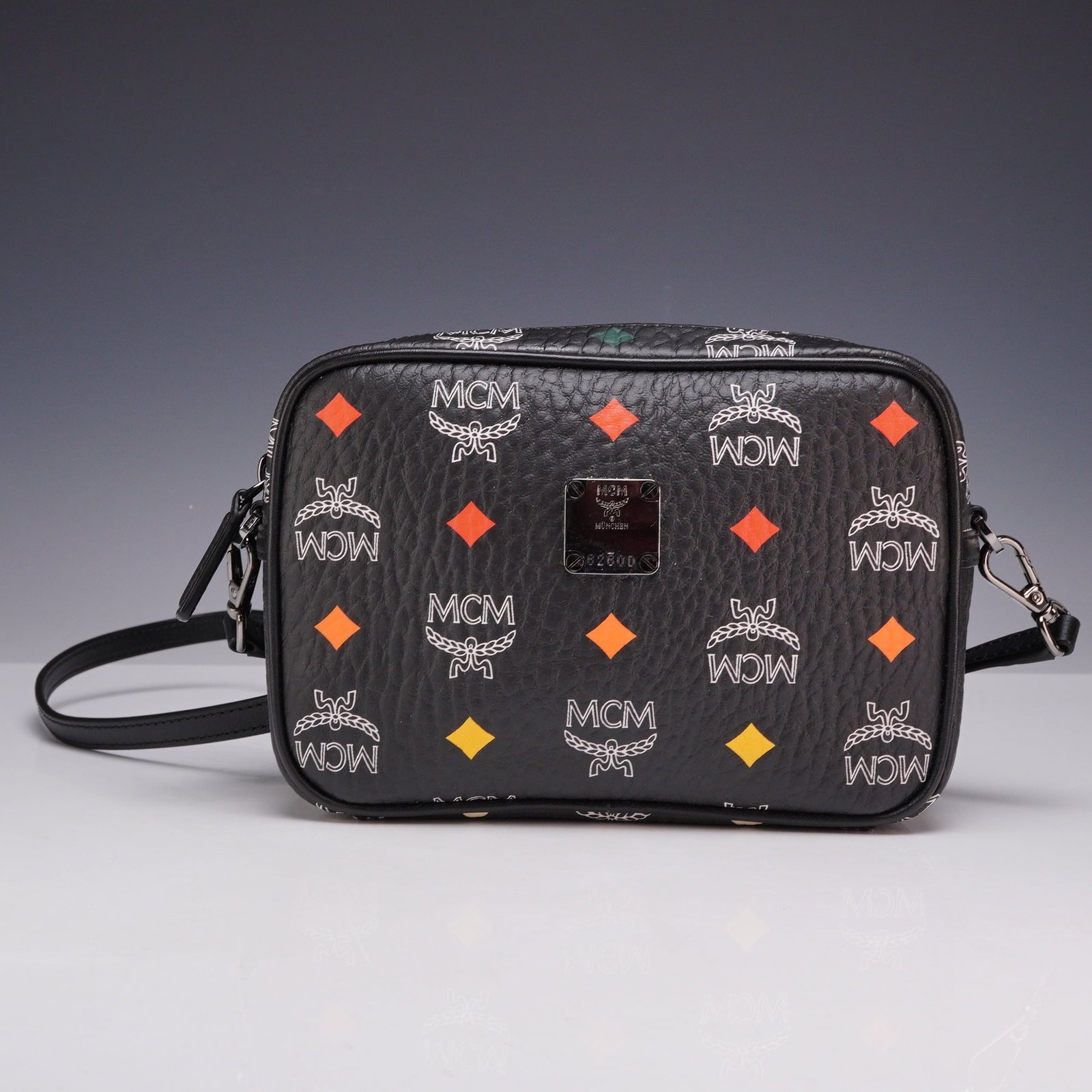 MCM Black Skyoptic Visetos Spectrum Diamond Camera Crossbody Bag: An MCM camera-style crossbody bag featuring the Skyoptic Visetos Spectrum Diamond pattern. The bag is constructed from black pebbled leather with a printed monogram design consisting of white MCM logo