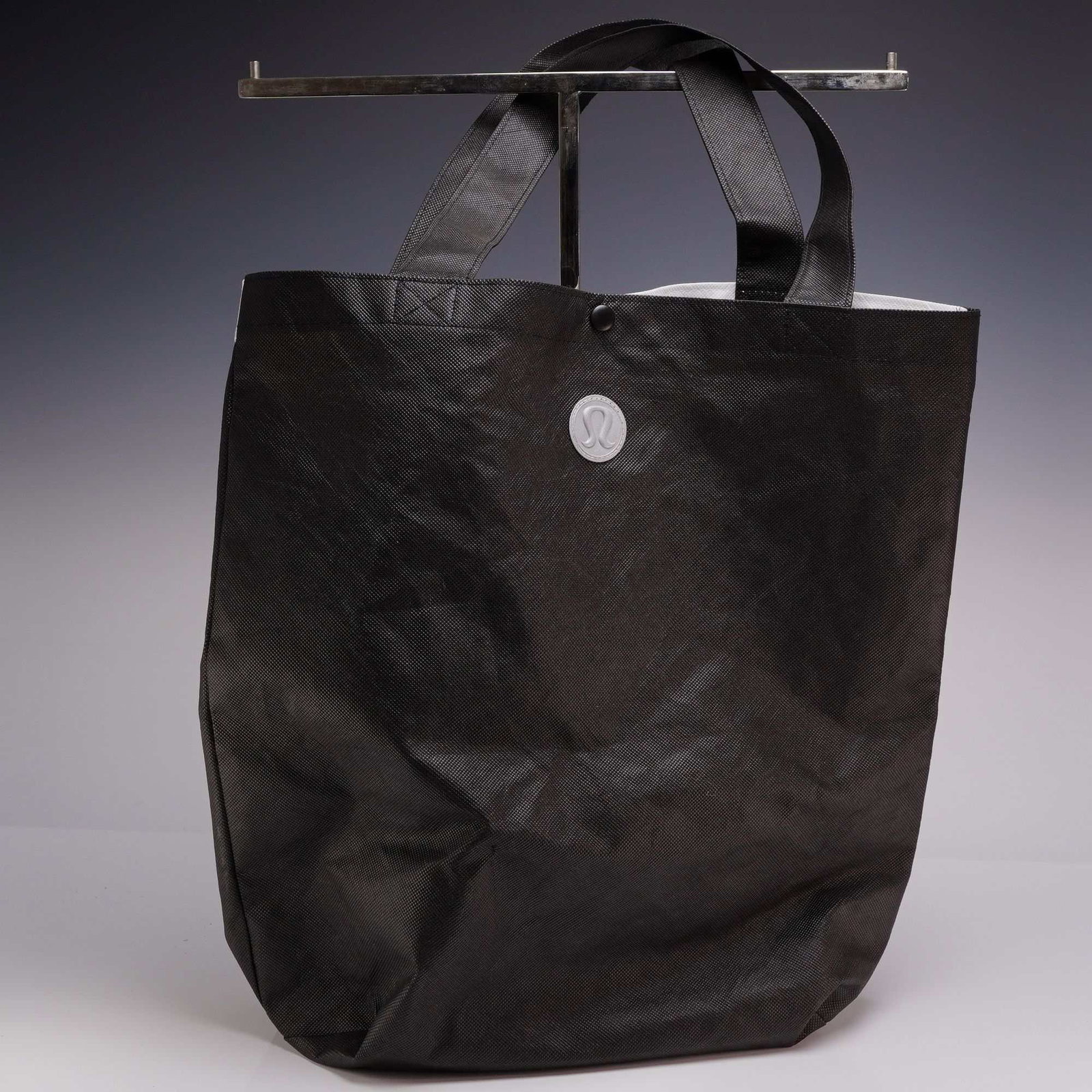 Lululemon Large Reusable Tote Carryall Gym Bag: A Lululemon Large Reusable Tote Carryall gym bag constructed from a durable, textured non-woven polypropylene synthetic textile. The tote features a solid black front face adorned with a centrally loc