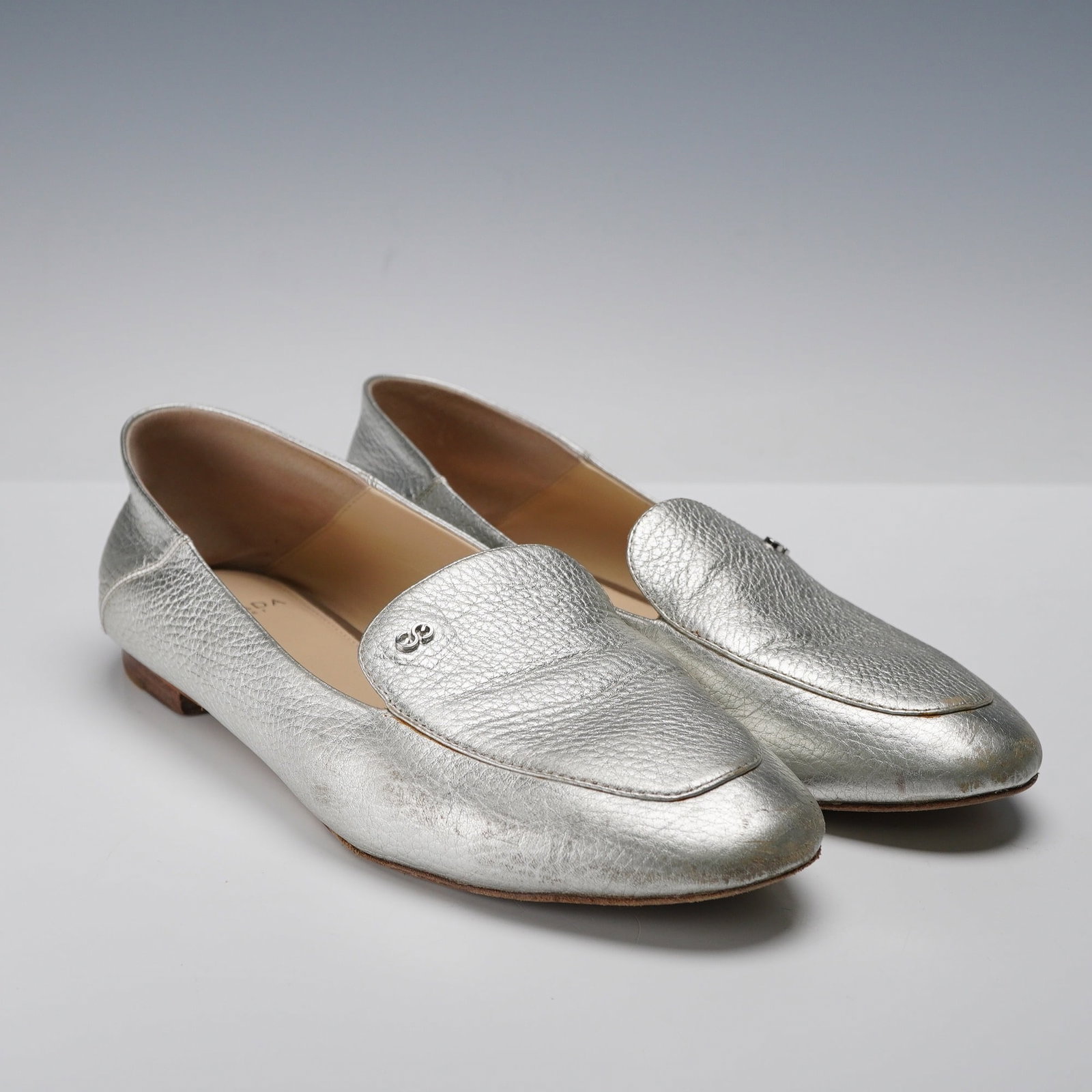 Pair of Escada Sport Leather Silver Flats: A pair of Escada Sport Silver Flats. These women's slip-on loafers feature a metallic silver-colored, textured leather finish. Each shoes upper is adorned with a small, metallic double-circle emblem. 