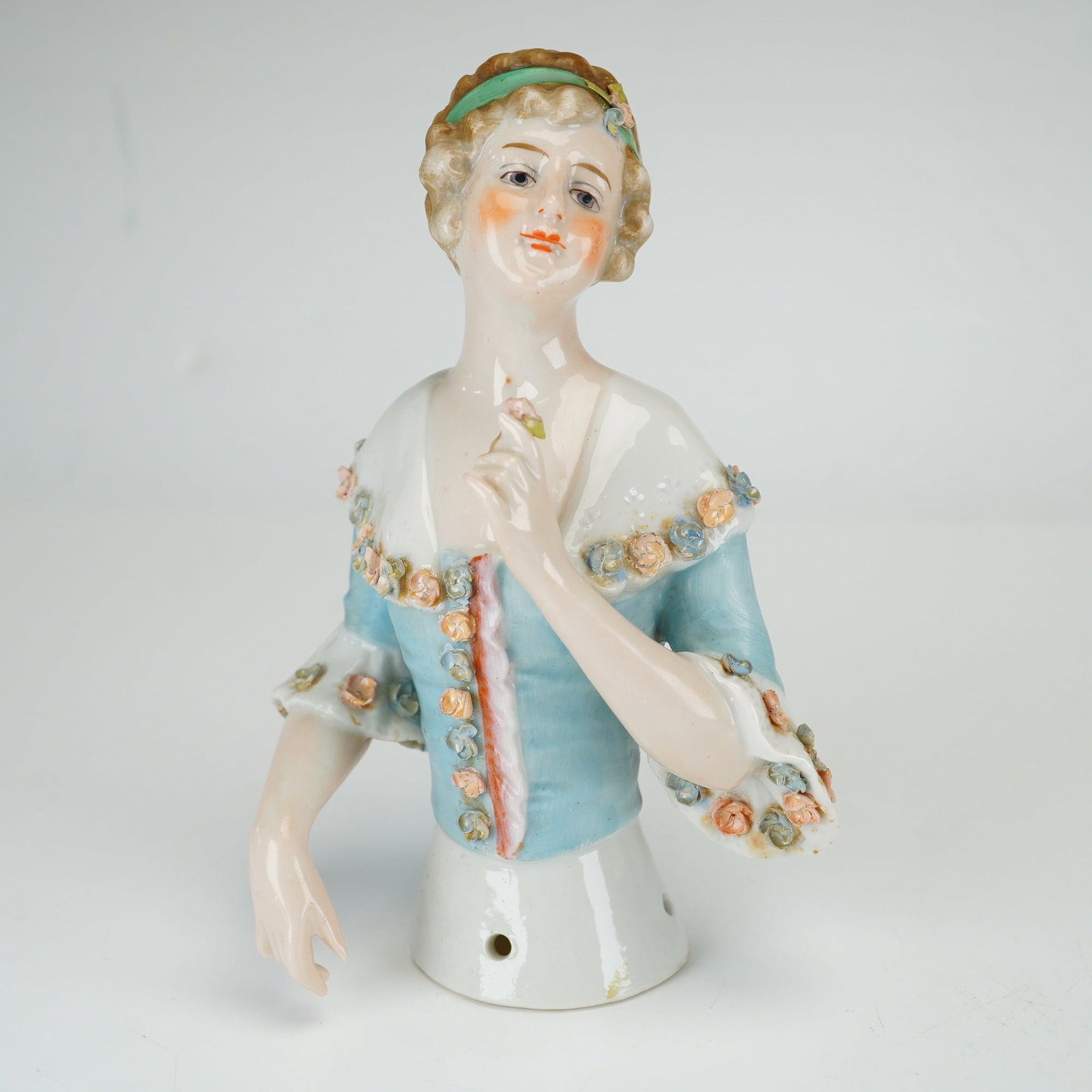 German Porcelain Half Doll with Applied Flowers: This German porcelain half doll is modeled as a woman in 18th-century style dress. The figure features a light blue bodice with a white fichu and ruffled sleeves, decorated with applied three-dimensio