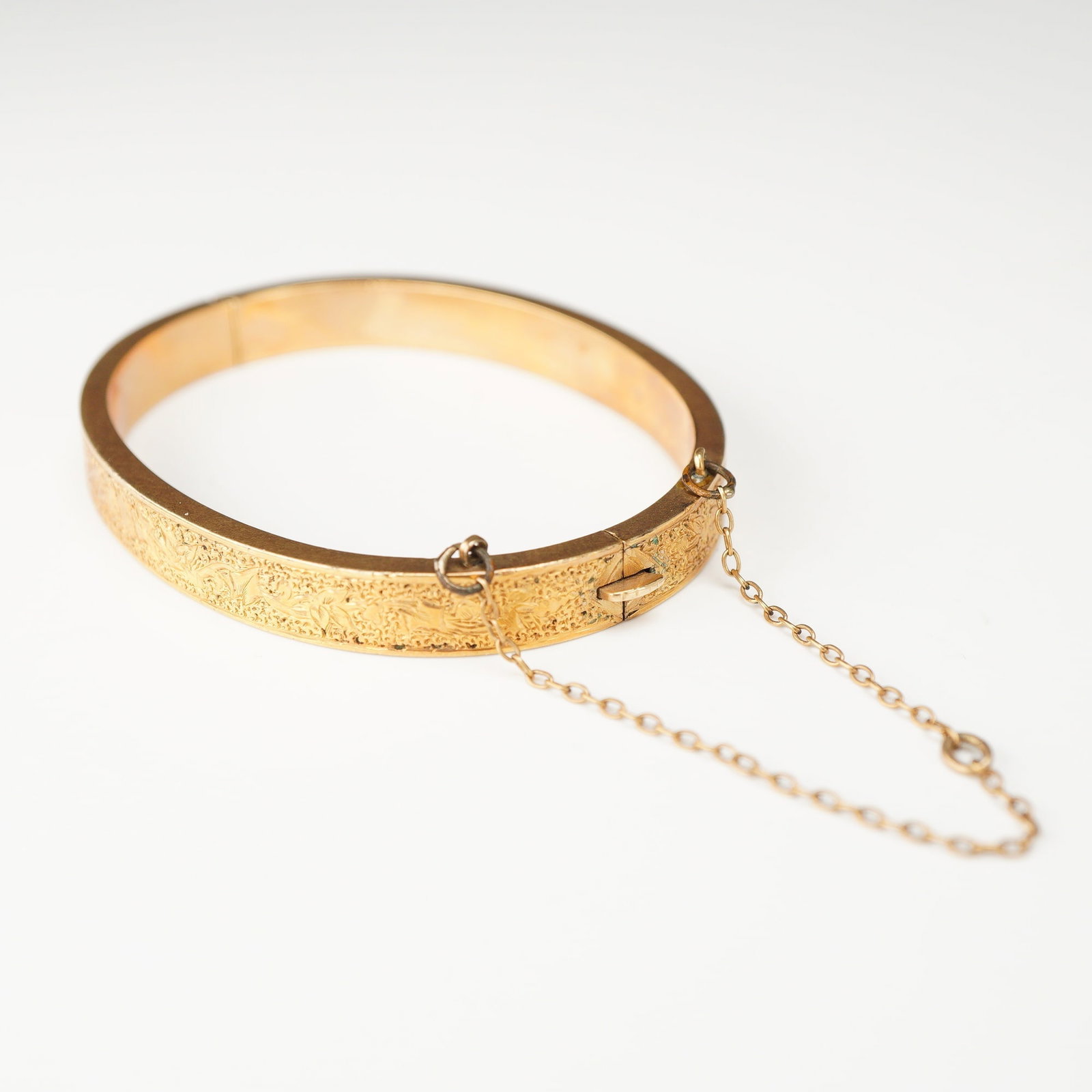 Victorian Style 16 Karat Yellow Gold Engraved Hinged Child Bracelet: The exterior of the band features an engraved floral and scrolling foliate pattern set against a stippled, textured background. The interior surface is polished. The bracelet is designed with a box cl