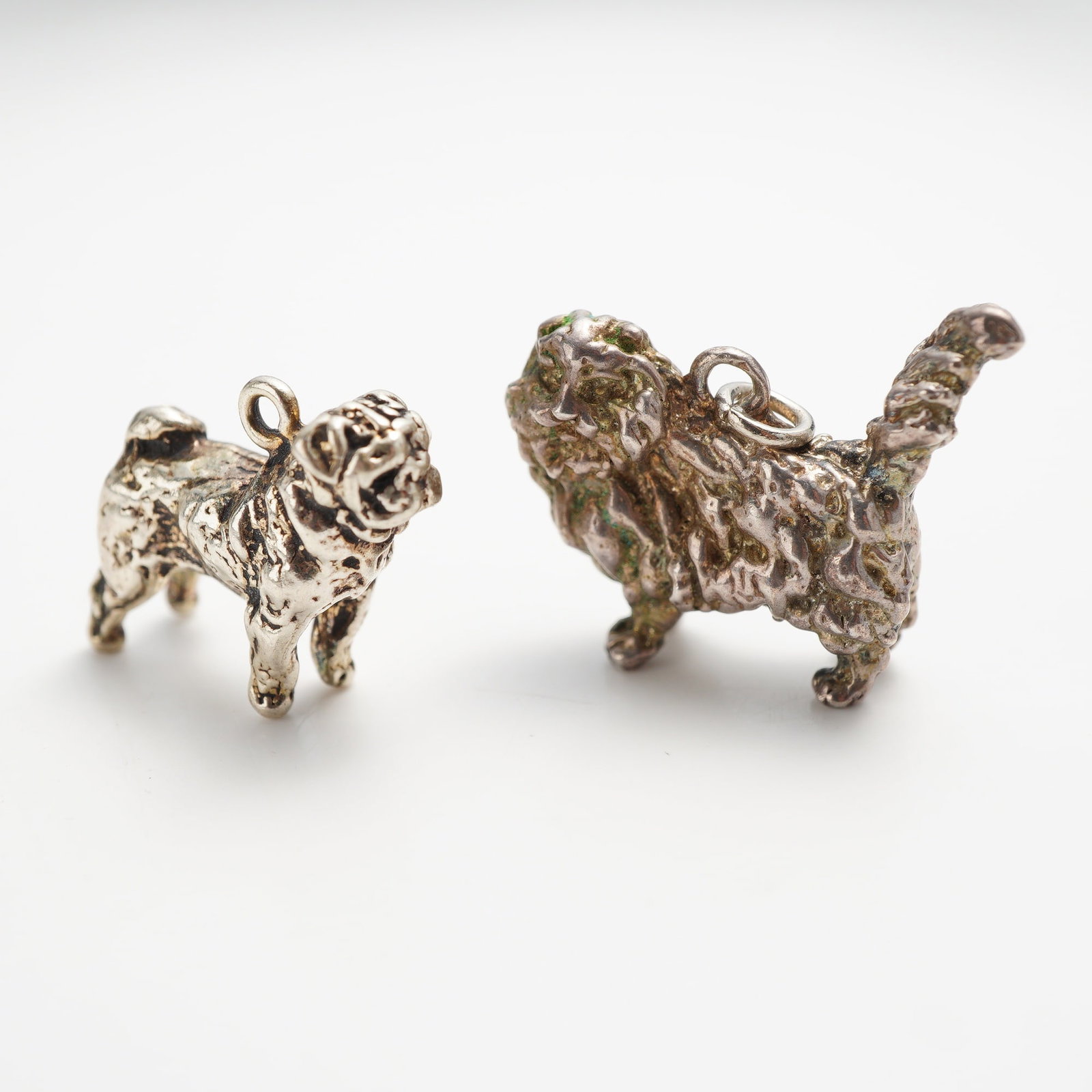 2pc Sterling Silver 925 Dog Charms: This pair of cast three-dimensional jewelry charms depicts two distinct dog breeds. One charm is modeled as a pug featuring characteristic facial wrinkles and a curled tail. The second charm depicts a