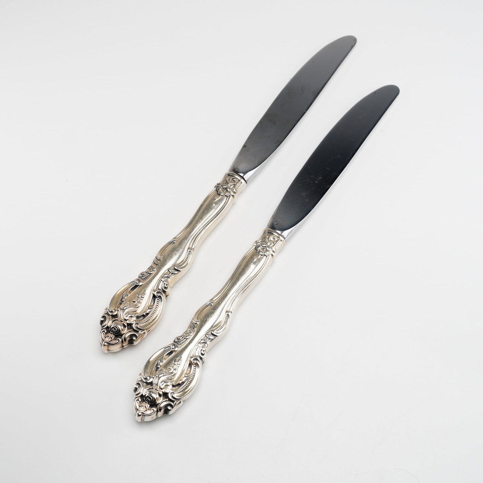 2pc Gorham Sterling Silver and Stainless Steel Dinner Knives, La Scala: A pair of sterling silver flatware knives in the La Scala pattern, manufactured by the Gorham Manufacturing Company. The handles feature an ornate Rococo-revival design characterized by intricate pier