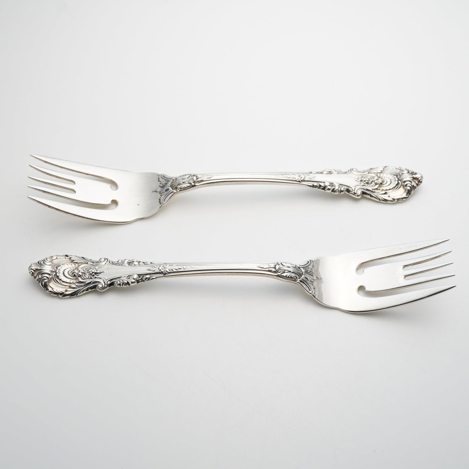 A Pair of Wallace Sterling Silver Salad Forks in the Sir Christopher Pattern: This pair of sterling silver salad forks is manufactured by Wallace Silversmiths in the Sir Christopher pattern. Introduced in 1936, the design features ornate relief work in the English Baroque style