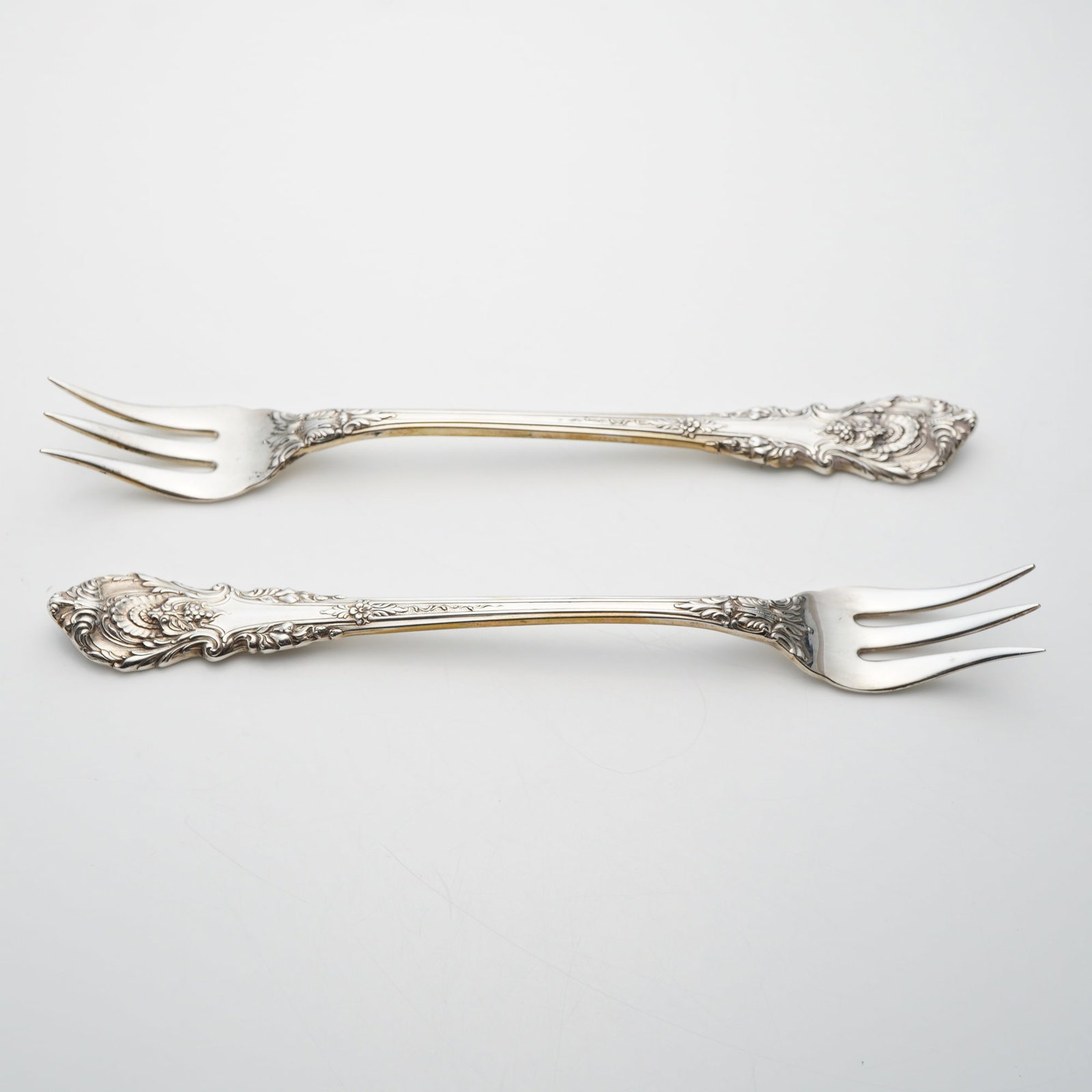 A Pair of Wallace Sterling Silver Sir Christopher Pattern Cocktail Forks: A pair of American sterling silver cocktail or seafood forks produced by Wallace Silversmiths in the Sir Christopher pattern. Introduced in 1936, this ornate Renaissance-style pattern features handles