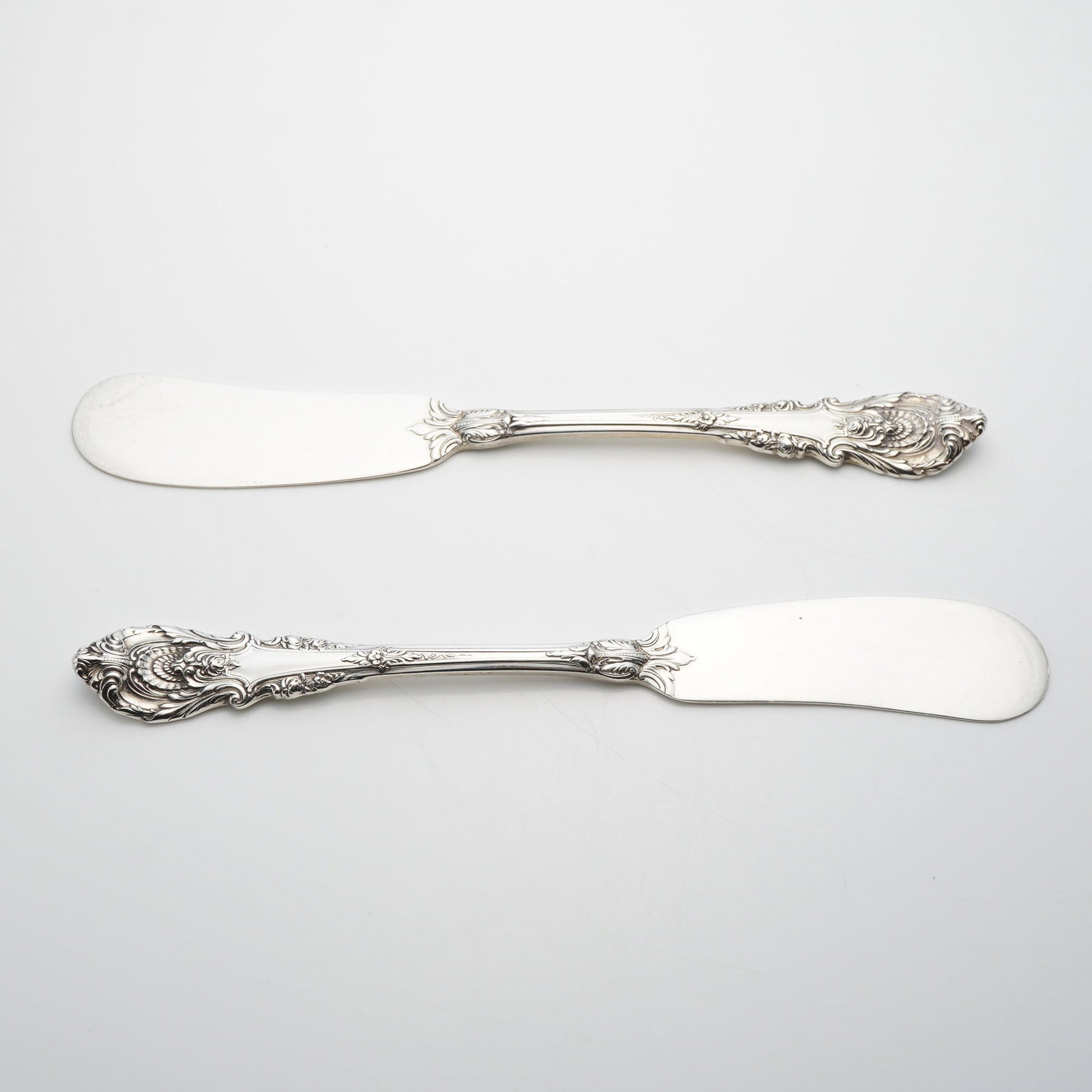 A Pair of Wallace Sterling Silver Sir Christopher Pattern Flat Handle Butter Spreaders: This lot consists of two flat handle butter spreaders in the Sir Christopher pattern by Wallace Silversmiths. Each piece is crafted from sterling silver and features a wide paddle-style blade. The han