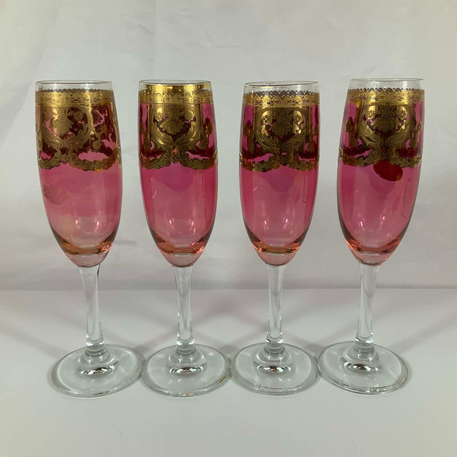 A Set of Four Vintage Italian Pink Glass Champagne Flutes with Gold Gilt Overlay: A set of four champagne flutes in the Venetian style, attributed to 20th-century Italian production. Each flute features a tapered bowl of cranberry-pink glass joined to a clear glass stem and a simpl