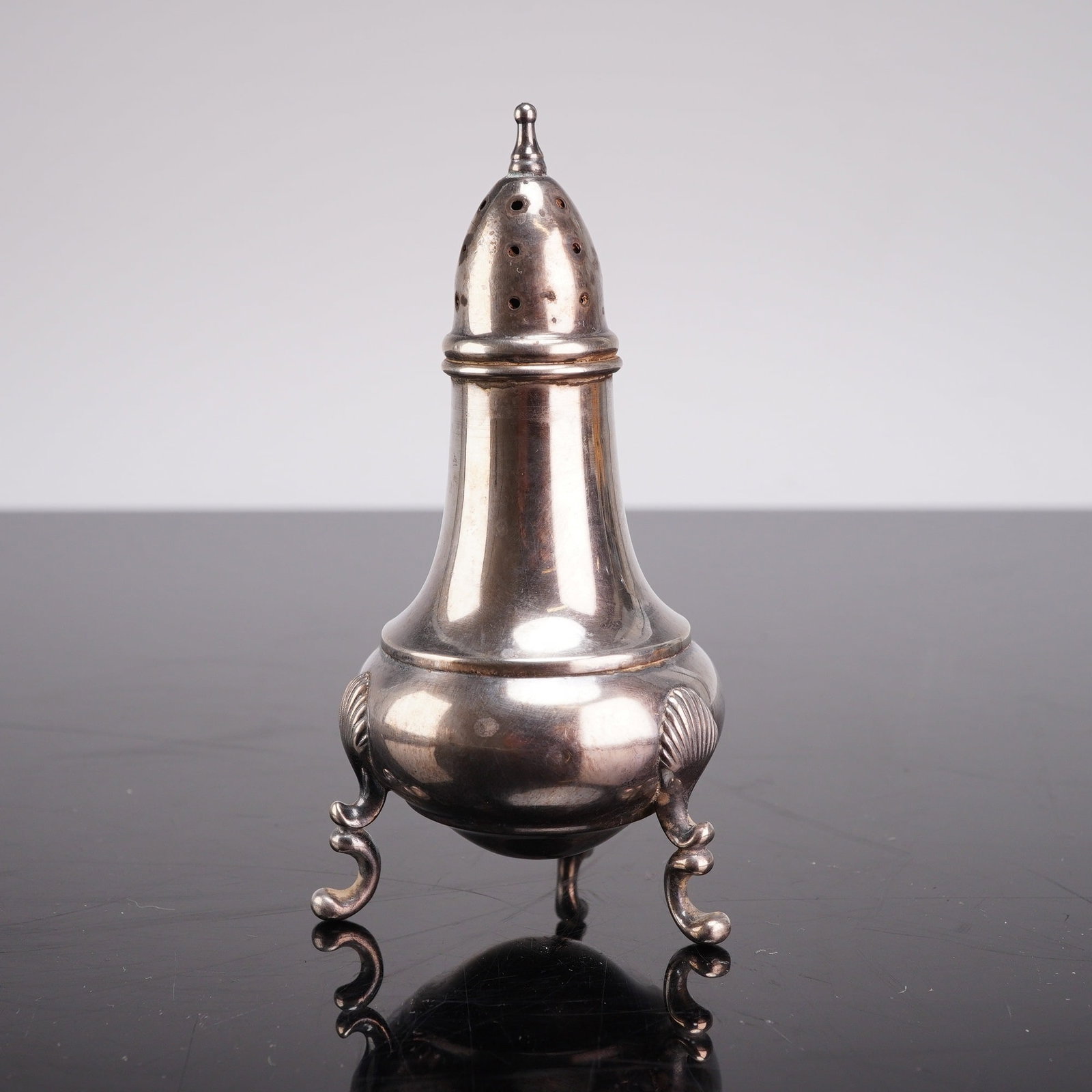 Sterling Silver Baluster Form Shaker on Scrolled Feet: A sterling silver shaker featuring a baluster-form body. The lower portion of the vessel is bulbous and tapers toward a narrow neck. It is fitted with a domed, perforated lid topped by a small pointed