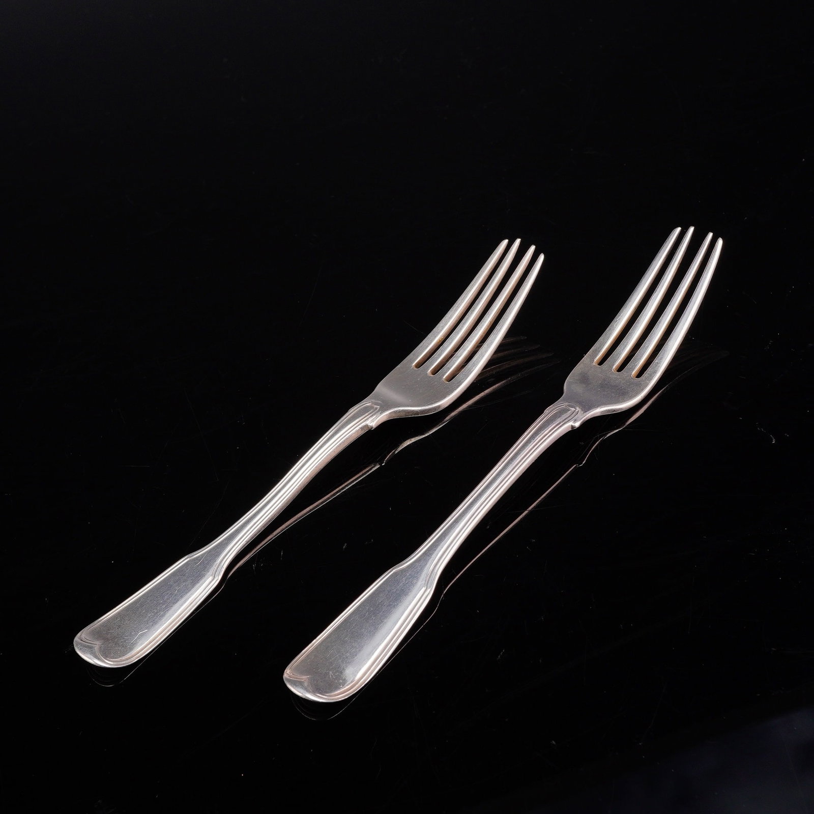 A Pair of Sterling Silver Fiddle Pattern Dinner Forks: This pair of sterling silver dinner forks is designed in the classic Fiddle pattern, a staple of English flatware characterized by its broad, flared handle ends and distinct shoulders at the base of t