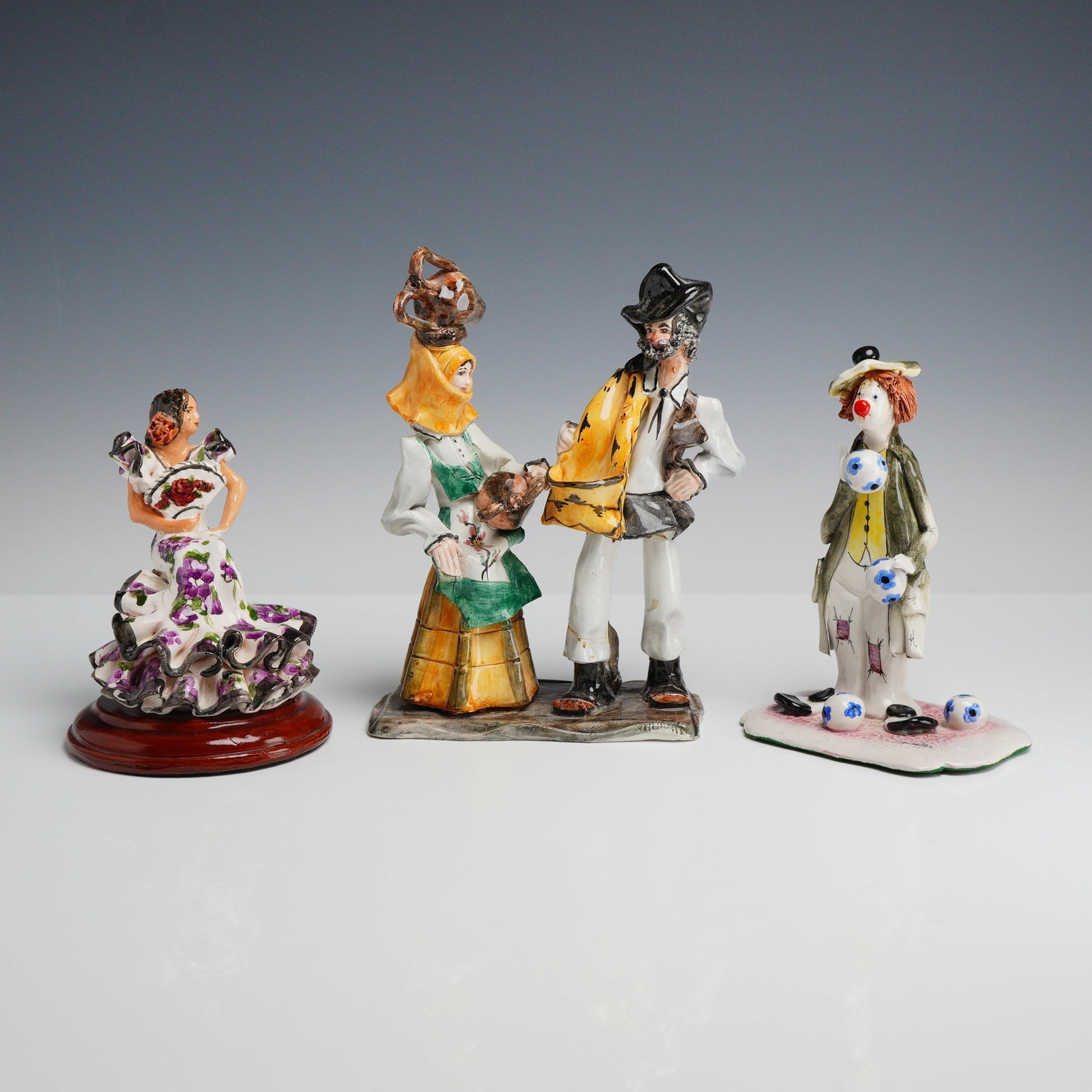 Three Hand Painted Ceramic Figurines including Stelio Mola and Zampiva: This collection consists of three handmade glazed ceramic figurines of Italian and European origin. The first is a Sardinian folk art sculpture by Stelio Mola, depicting a couple in traditional region