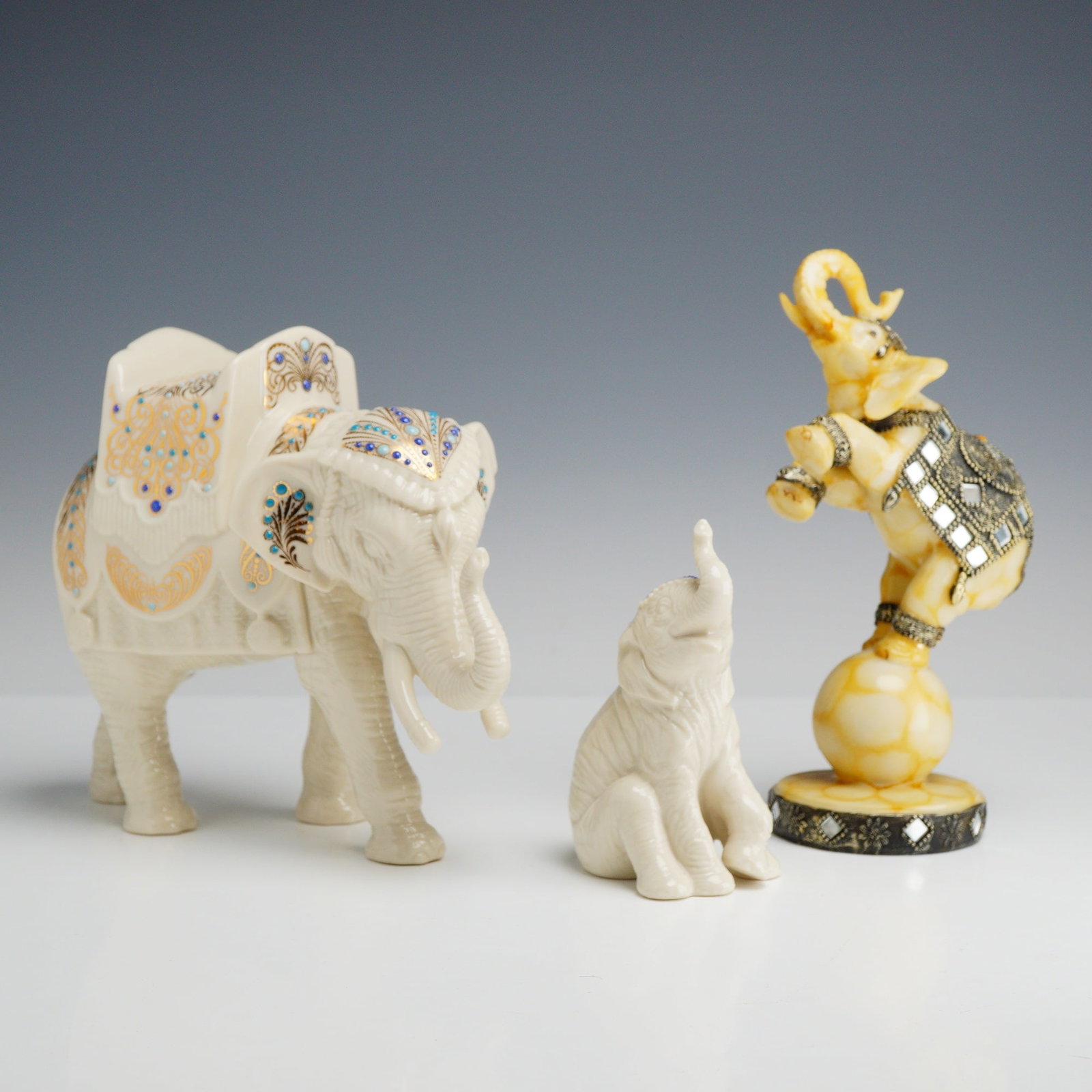 3pc Elephant Figurines Including Lenox China Jewels Porcelain: This collection consists of three decorative elephant figurines, including two pieces from the Lenox China Jewels collection and one unmarked performing elephant. The larger walking elephant is crafte