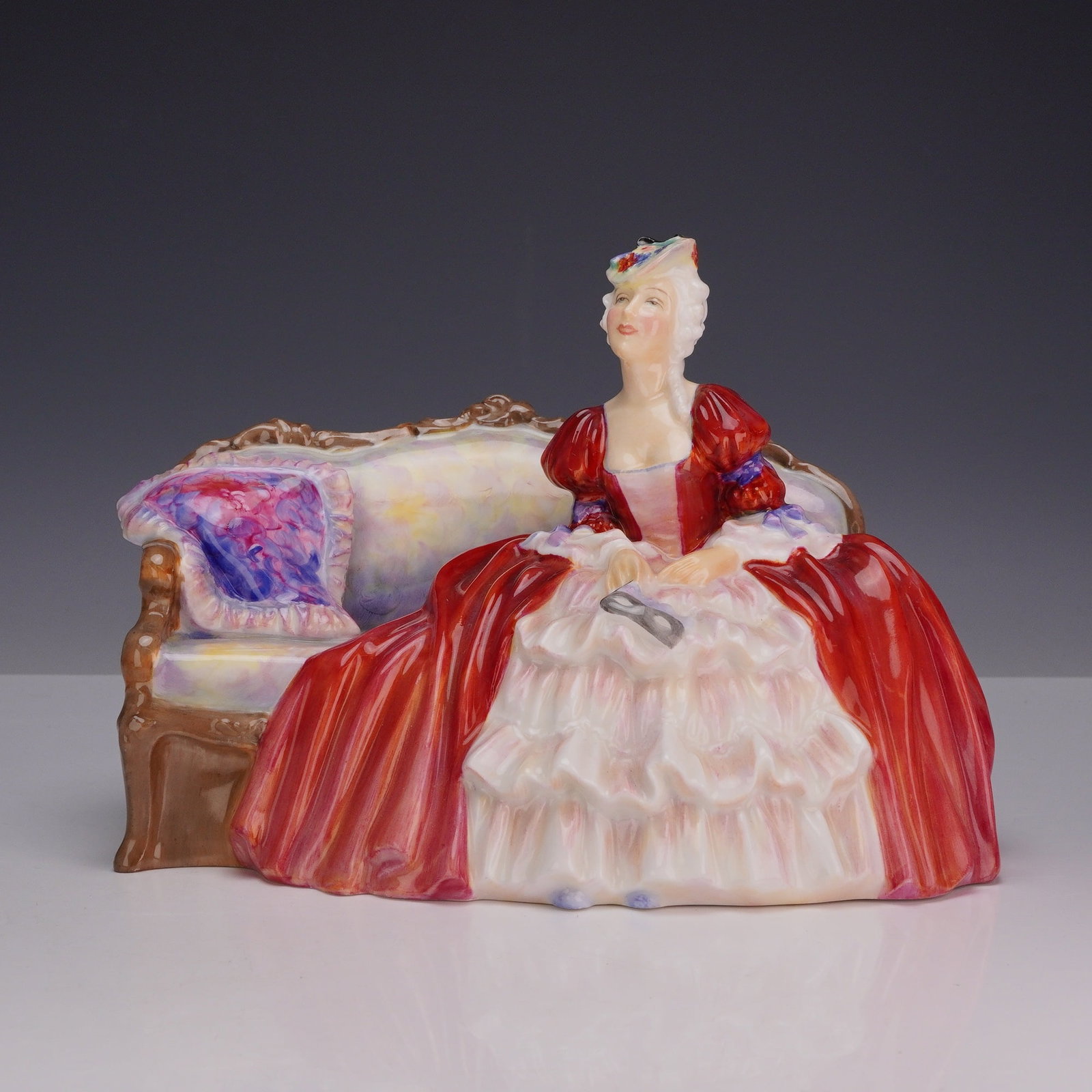 Royal Doulton Bone China Figurine, Belle O'The Ball HN1997: Designed by Roy Asplin, this hand-decorated Royal Doulton figure portrays an elegant lady seated gracefully upon a 19th-century style settee. She is dressed in a striking red gown, capturing the charm