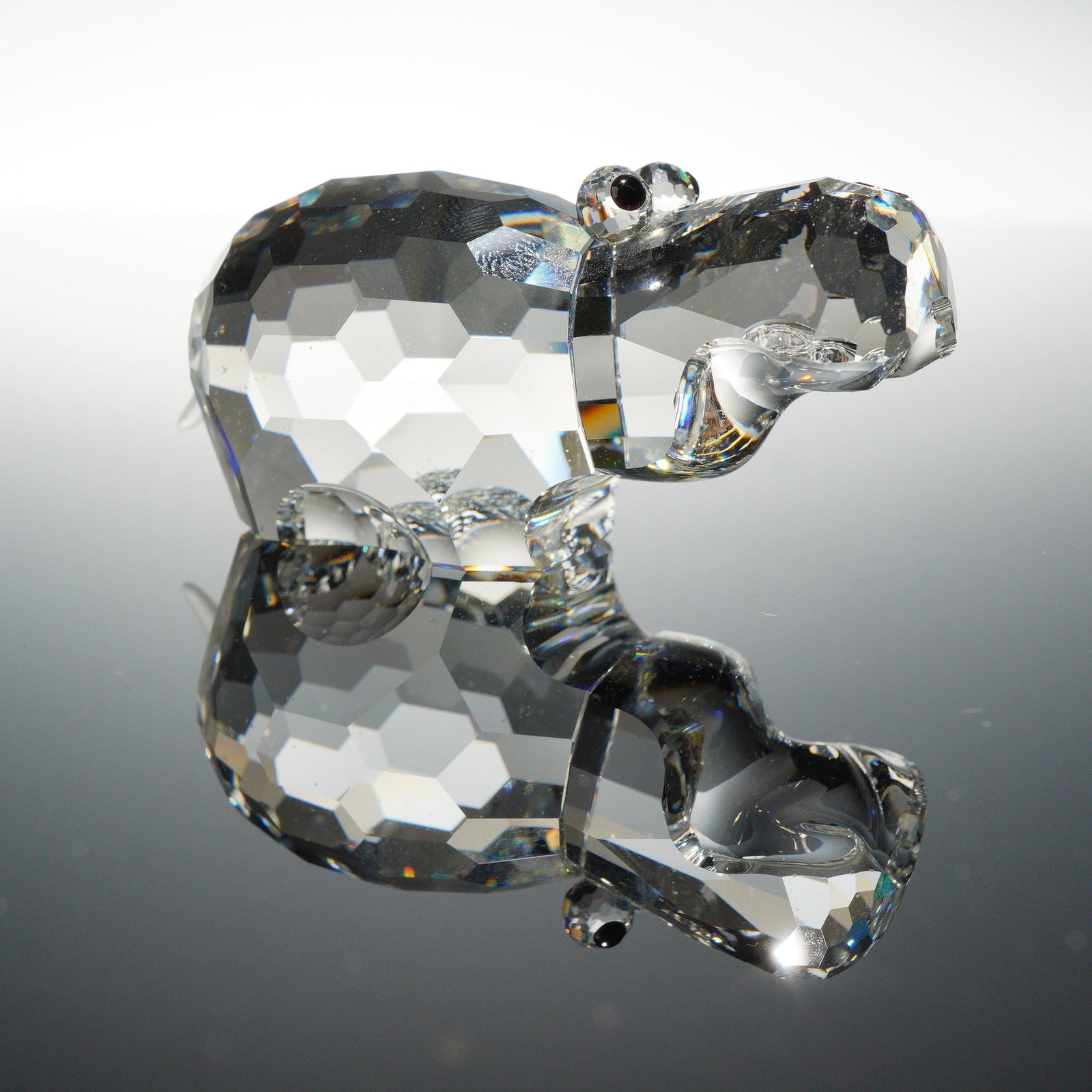 Swarovski Silver Crystal Hippo Figurine with Original Box: A Swarovski Silver Crystal hippopotamus figurine crafted from clear faceted lead crystal. The piece features a multifaceted body and head with two inset black crystal eyes and a small frosted crystal 
