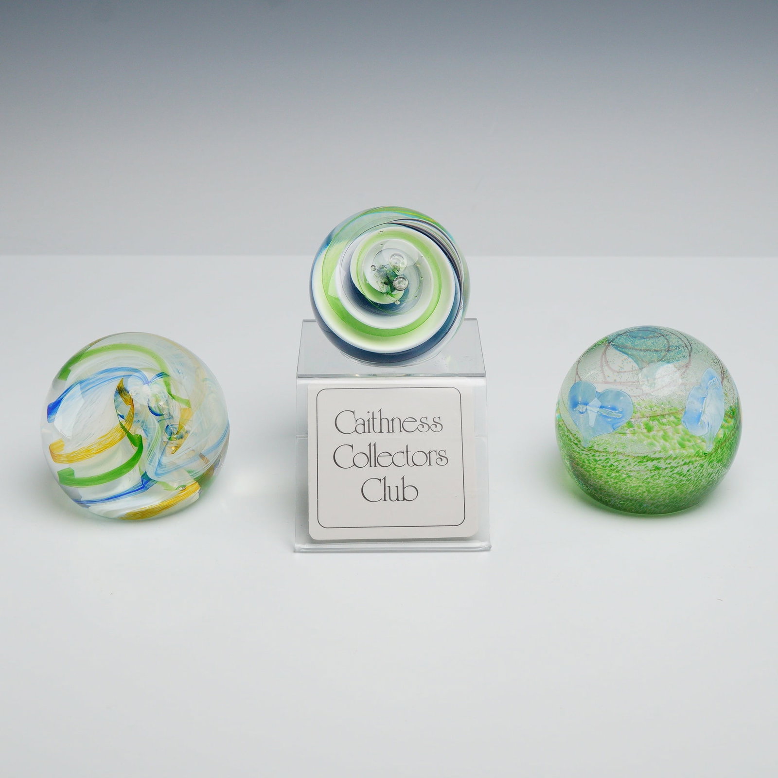 3pc Caithness Art Glass Paperweights, Summer Breeze, Dizzy, and Ribbons: This lot comprises a trio of hand-blown Caithness Glass paperweights from Scotland, featuring the designs Summer Breeze, Dizzy, and Ribbons, accompanied by two original presentation boxes and a Caithn