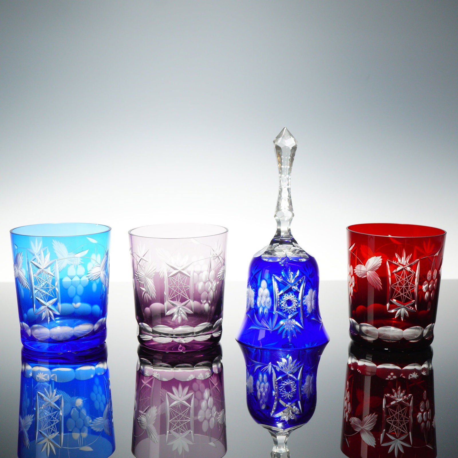 Lot of 4 Colored Cut-to-Clear Crystal Items: This lot features 4 pieces of colored cased-to-clear crystal, including three tumblers and one decorative bell. The pattern features a central hobstar motif contained within a rectangular geometric fr
