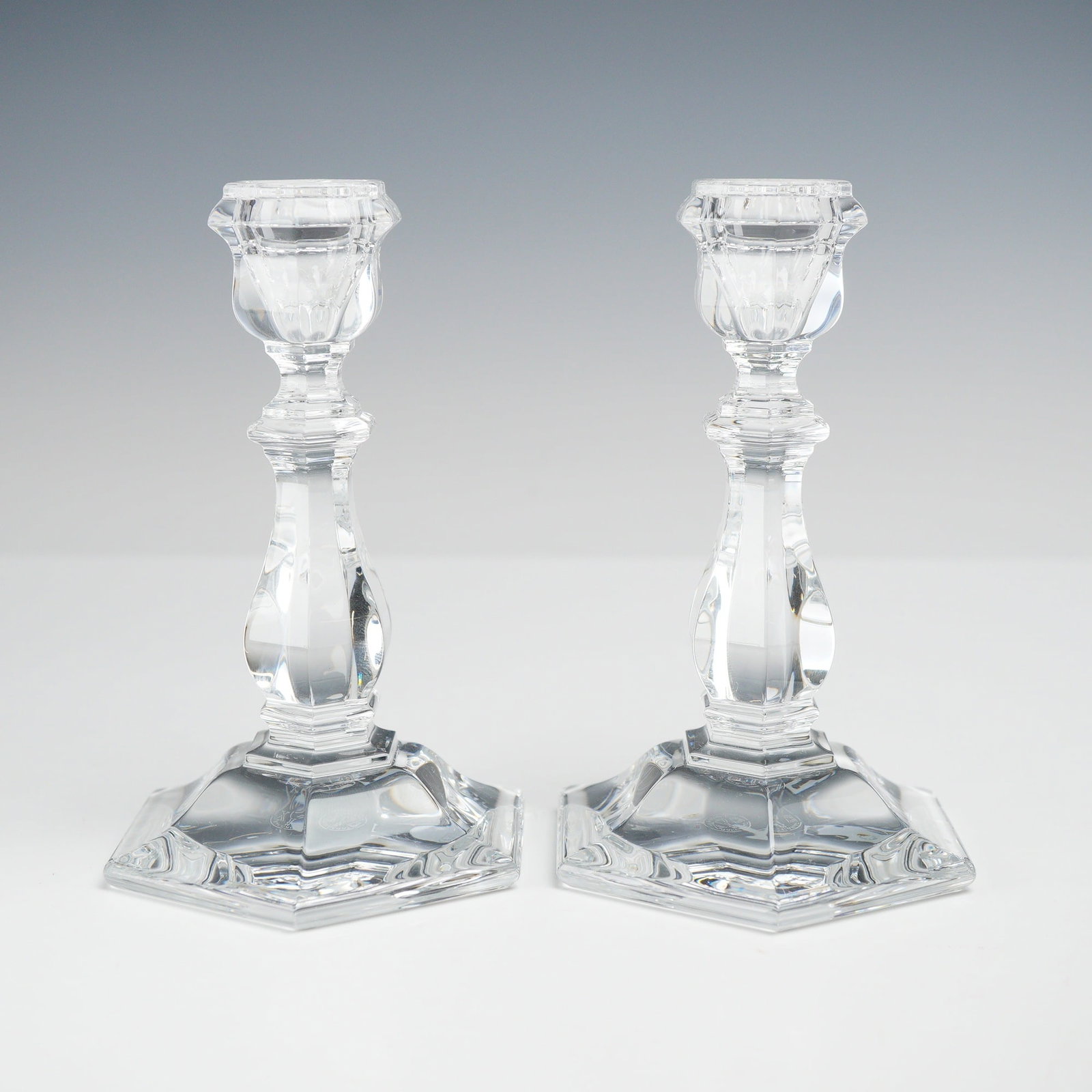 A Pair of Baccarat Vestale Crystal Candlesticks: This Baccarat candle holder set of 2 is executed in the Vestale pattern. Constructed from heavy, high-quality clear lead crystal, each candlestick features a broad hexagonal base, a multi-faceted stem