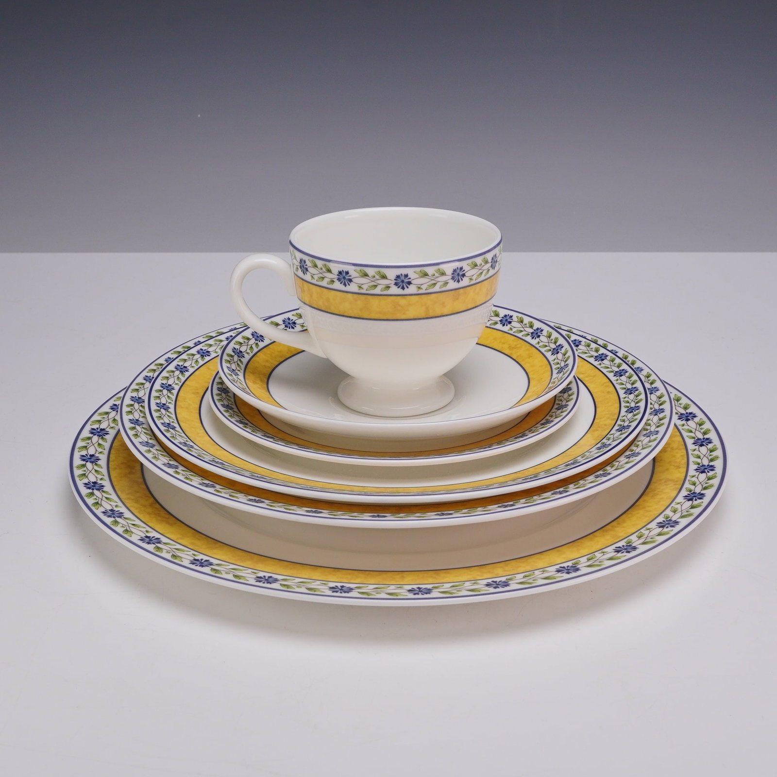 6 Piece Set of Wedgwood Bone China Plates and Teacup, Mistral: A set of six Wedgwood bone china dinnerware items in the Mistral pattern. This collection contains multiple plates and a teacup. The pattern is defined by a textured yellow band flanked by thin blue l