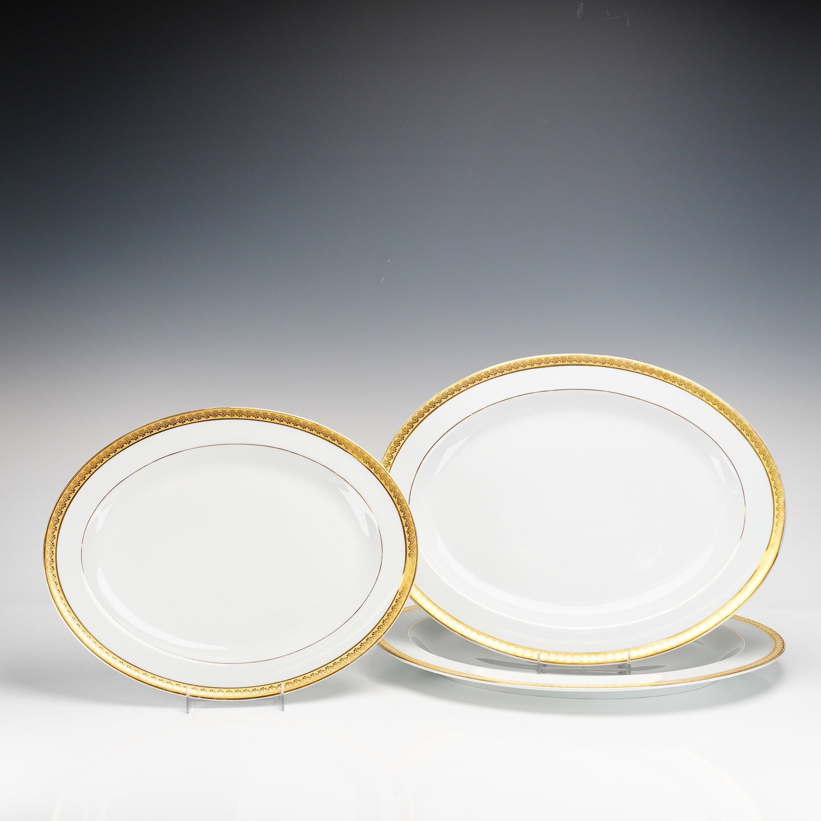 Three Bernardaud Limoges France Graduated Oval Serving Platters, Rhapsody Porcelain: Each piece is constructed from fine white porcelain. The decoration features a wide, acid-etched gold rim with an intricate repeating geometric and foliate motif. The inner edge of the gold border is 