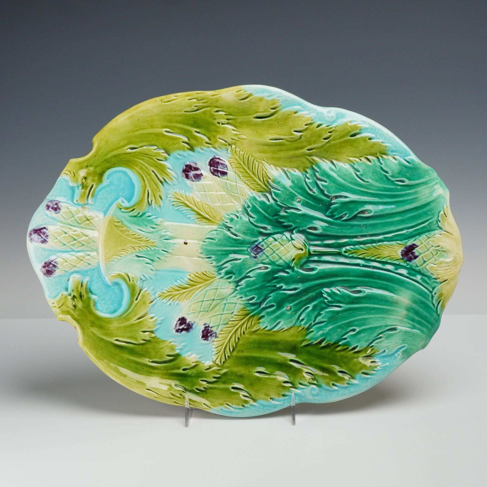 Late 19th Century Majolica Asparagus Serving Platter: This relief-molded earthenware platter features a vibrant polychrome lead glaze characteristic of Victorian-era majolica. The oval form is decorated with a central composition of large, sweeping acant