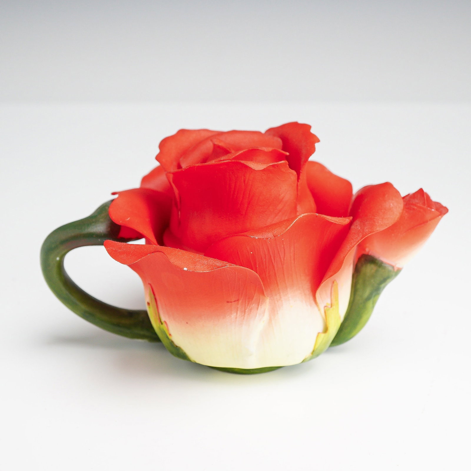 Cosmos Gifts Fine Porcelain Red Rose Lidded Teapot Figurine: A decorative ceramic miniature lidded vessel designed in the form of a blooming red rose, produced by Cosmos Gifts. The two-piece item consists of a main body formed by the outer petals of the flower 
