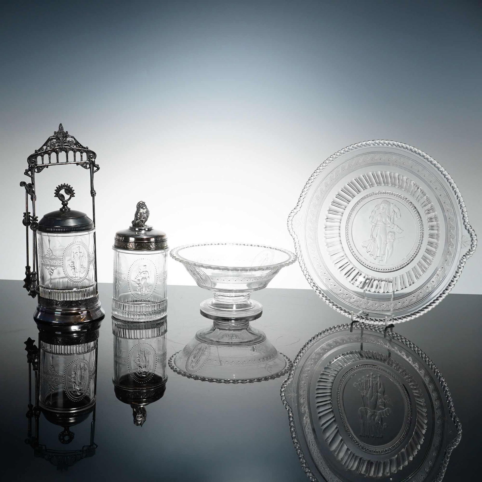 Lot of 4 Richards & Hartley Glass Pieces in the Cupid and Venus Pattern: This is a lot of 4 pressed glass pieces produced by Richards & Hartley in the Cupid and Venus pattern, circa late 19th century. The collection includes a pickling jar with a silver-plated stand and
