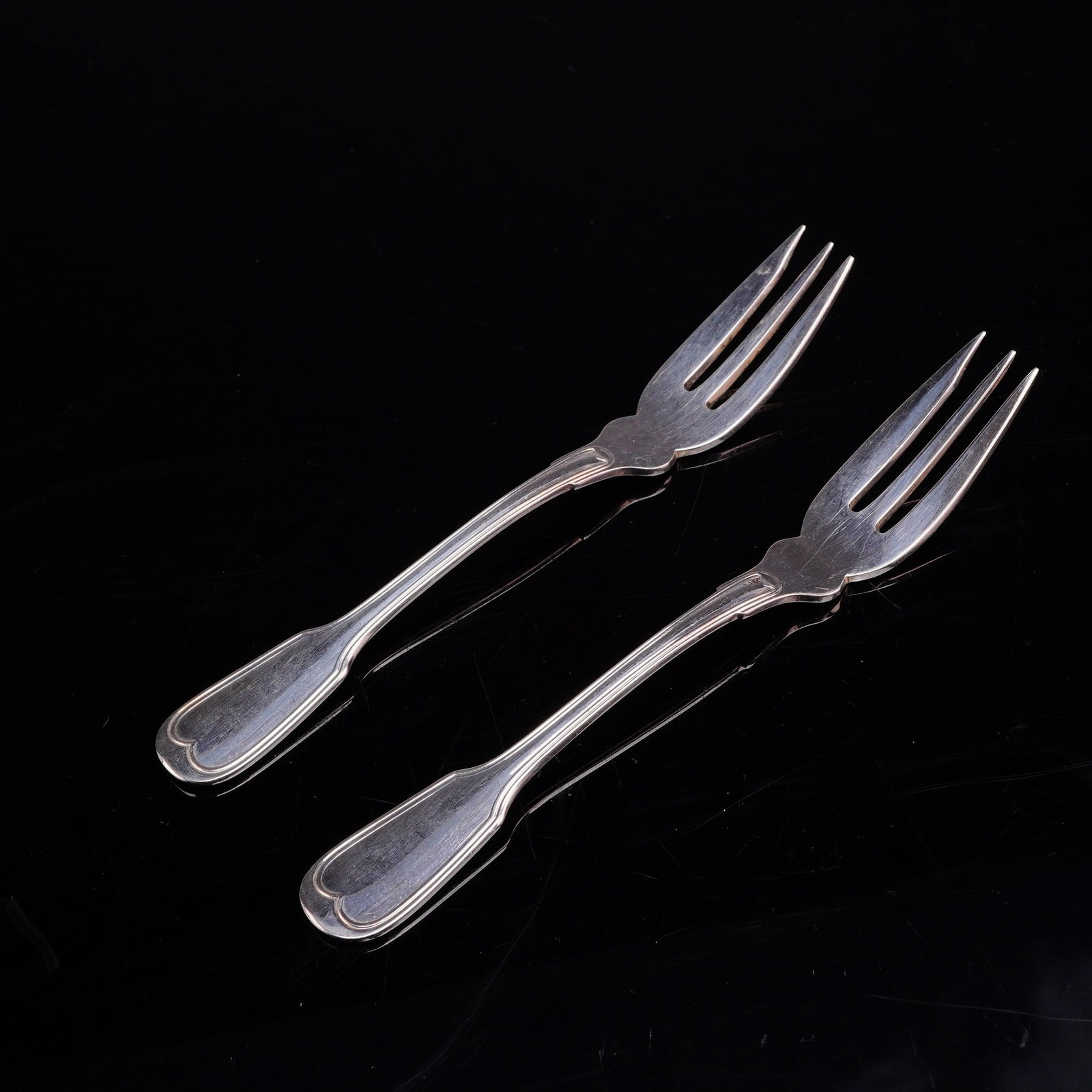 A Pair of Buccellati Nantucket Silver-Plated Cocktail Forks: A pair of silverplated three-tine forks in the Nantucket pattern by the Italian silversmith Buccellati. Each fork features a shaped handle with a double-fillet border terminating in a heart-shaped tip