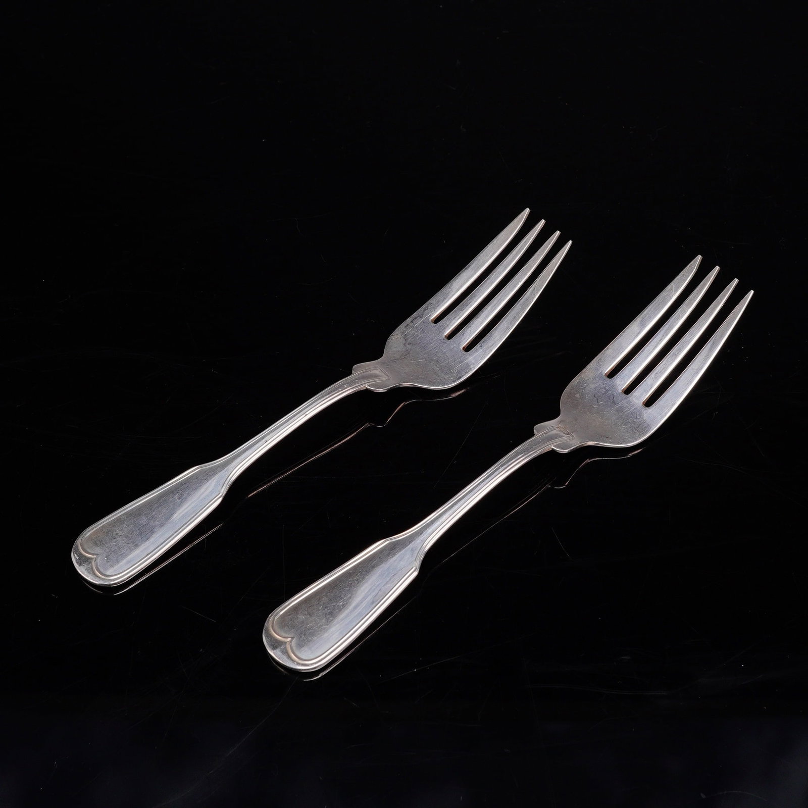 A Pair of Frank W. Smith Silver Co. Sterling Silver Forks in the Fiddle Thread Pattern: A pair of sterling silver forks manufactured by Frank W. Smith Silver Co. Each fork is designed with a fiddle-shaped handle that terminates in a double-scroll motif forming a heart-like shape. The for