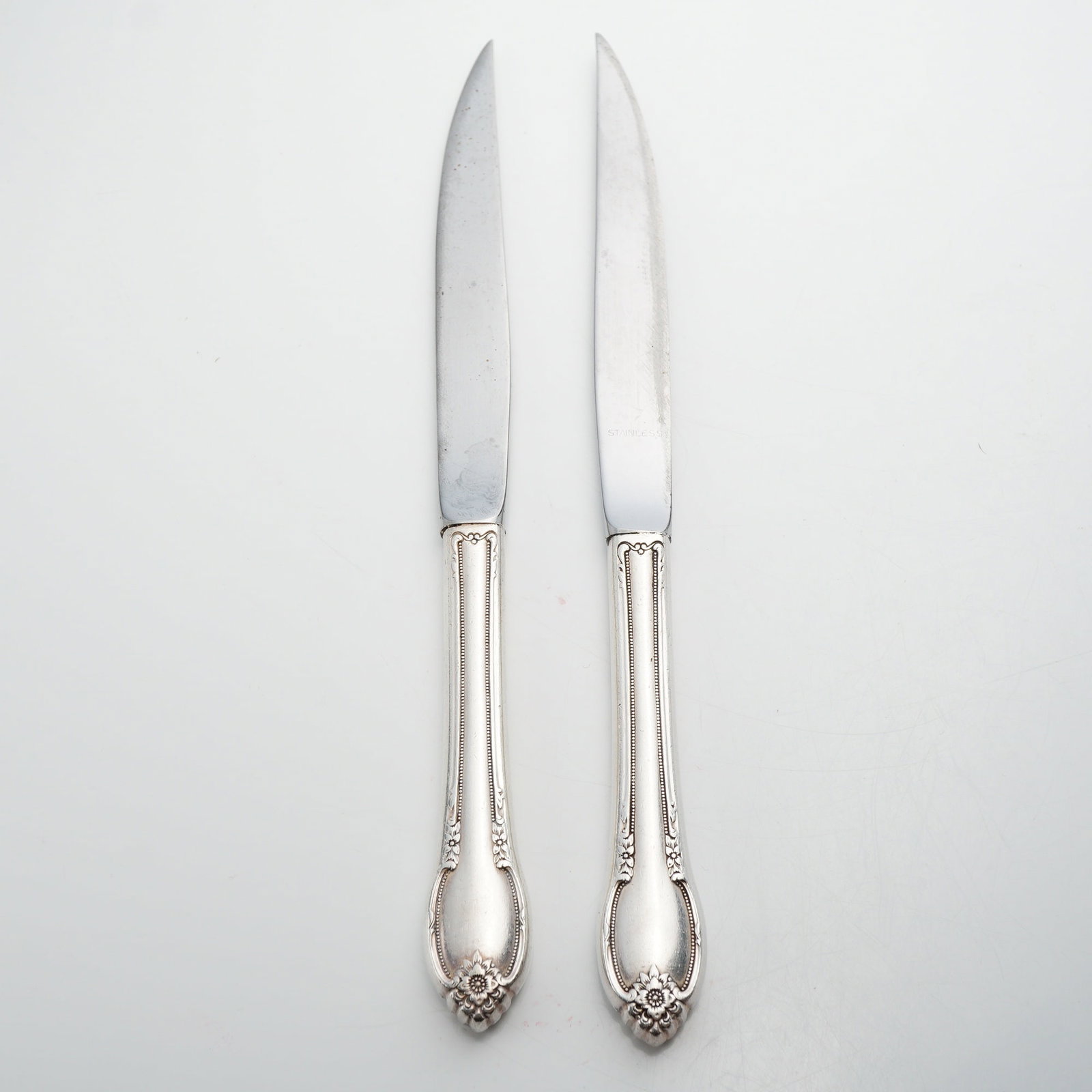 Two Sterling Silver Handled Knives with Floral and Scroll Decoration: These two knives feature hollow-constructed sterling silver handles and stainless-steel blades. The handles are decorated in the Joan of Arc pattern attributed to International Silver, characterized