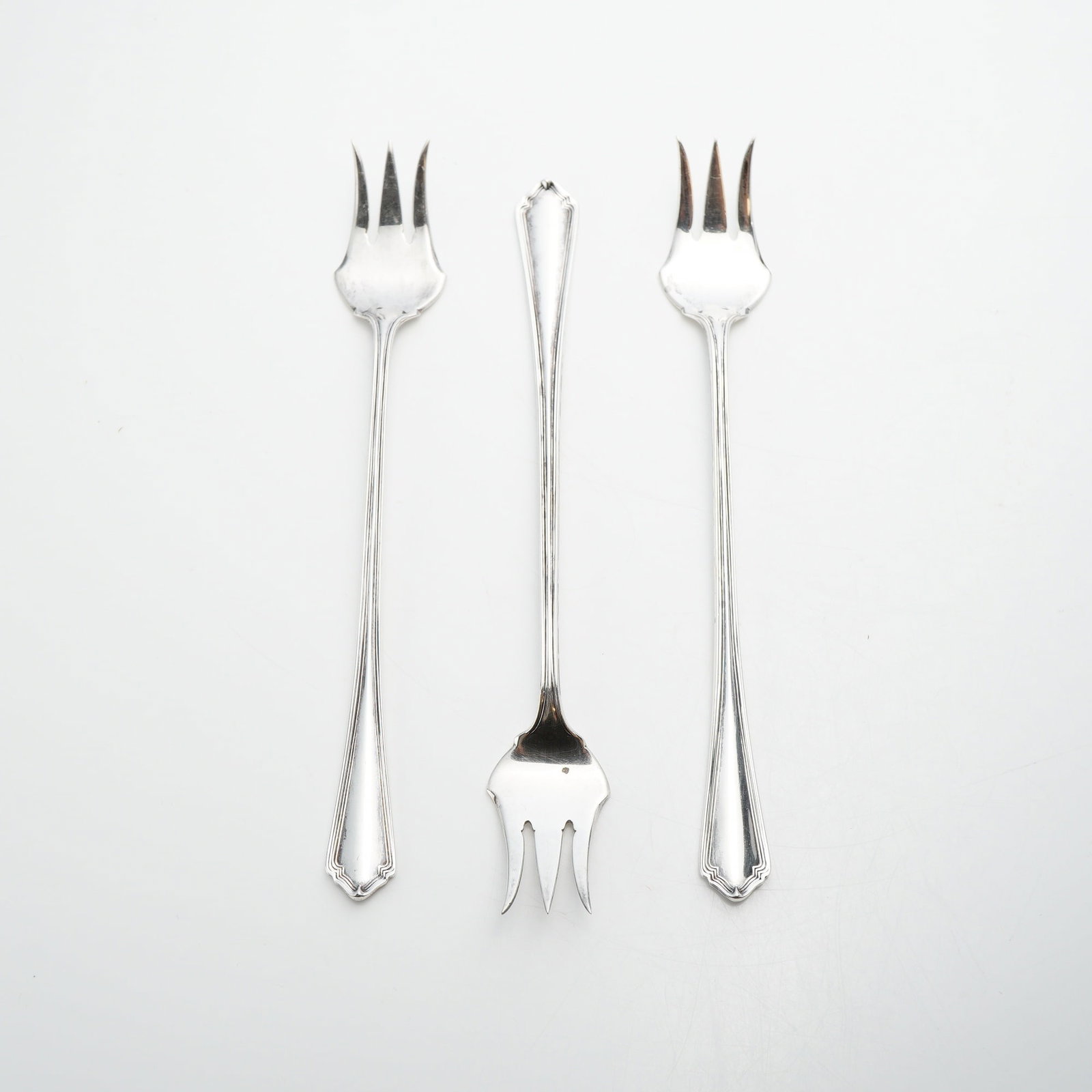 Lot of 3 Wallace Silversmiths Sterling Silver Cocktail Forks: A lot of three sterling silver cocktail or seafood forks manufactured by Wallace Silversmiths. Each fork is designed with a long, slender handle featuring a double-threaded border that terminates in