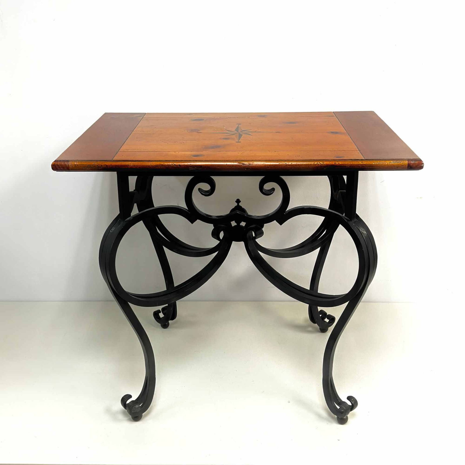 Baker Furniture Wrought Iron and Pine Accent Coffee Table with Compass Rose Inlay: This accent coffee table by Baker Furniture features a rectangular solid pine wood top supported by a decorative black-painted wrought iron steel base. The wooden top is constructed with breadboard