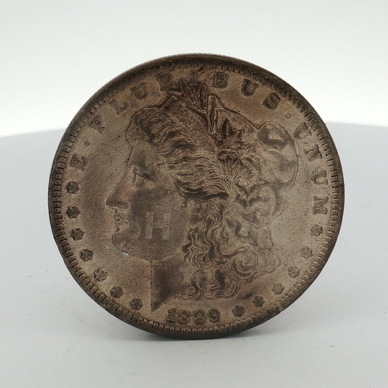 1889 US Morgan Silver Dollar Coin Circulated: This 1889 US Morgan silver dollar was struck at the Philadelphia Mint. The coin is composed of 90 percent silver and 10 percent copper. The obverse features the Liberty Head design surrounded by thirt