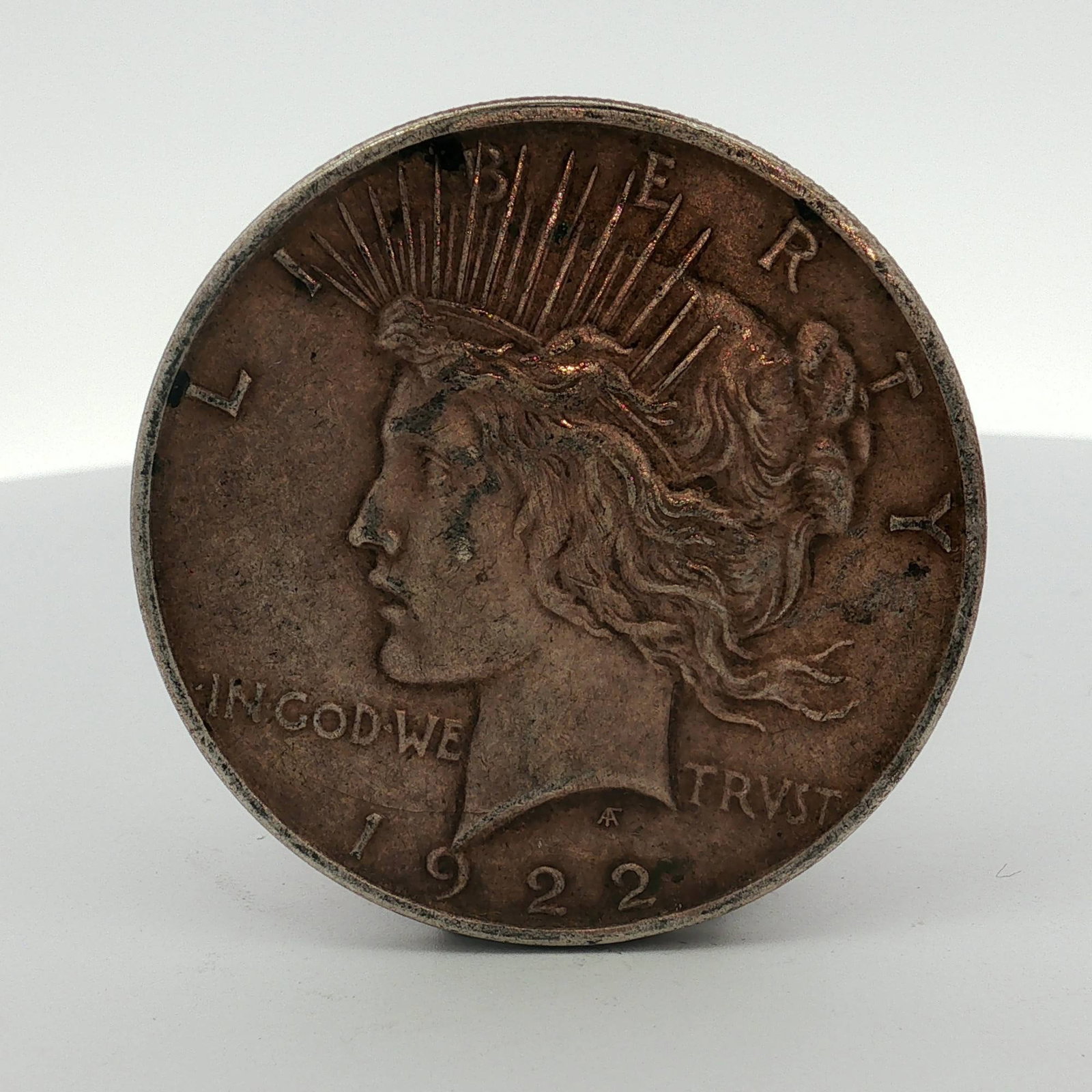 1922-D US One Dollar Peace Silver Dollar, Circulated: This Peace dollar is a 1922 US silver coin struck at the Denver Mint. The piece is composed of 90% silver and 10% copper. It features the standard Peace dollar design by Anthony de Francisci, with the