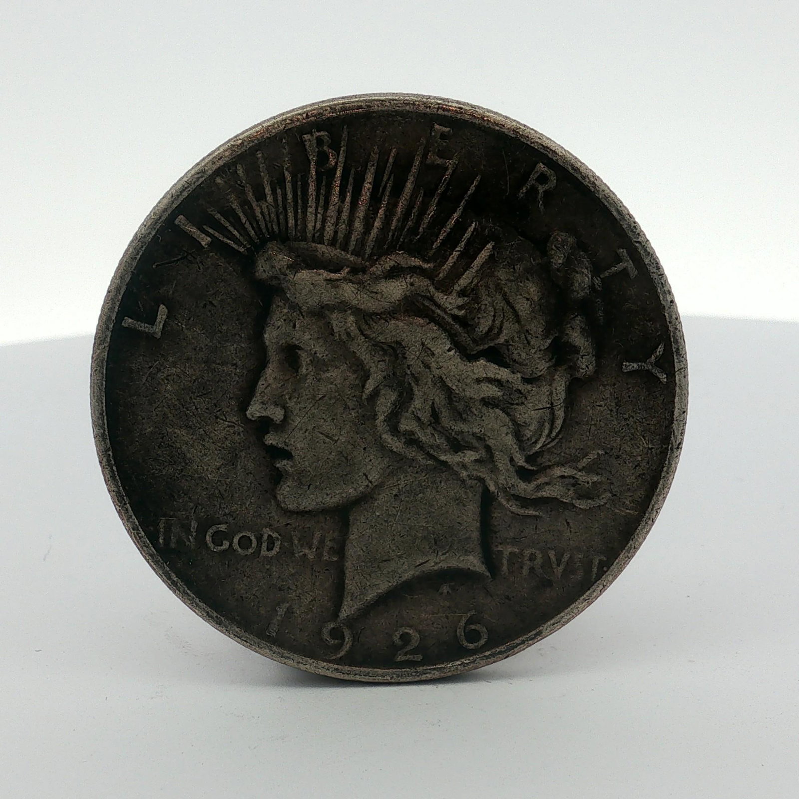 1926-D US One Dollar Peace Silver Dollar, Circulated: This US 1926-D Peace dollar is a 90 percent silver coin designed by Anthony de Francisci and struck at the Denver Mint. The obverse features the Liberty head design with inscriptions LIBERTY, IN GOD W