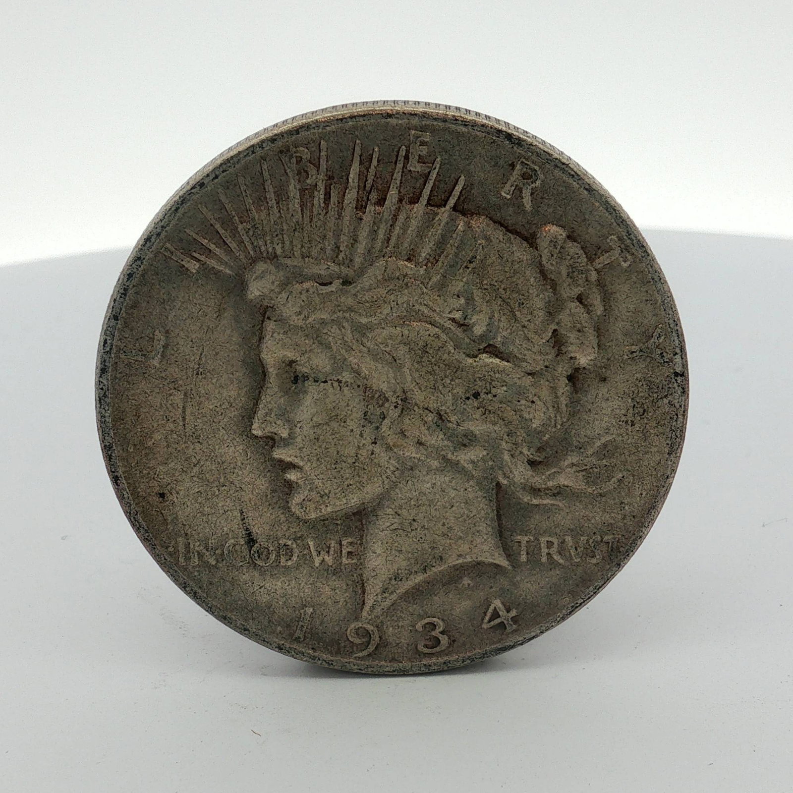 1934-D US One Dollar Peace Silver Dollar, Circulated: This US Peace dollar was struck at the Denver Mint in 1934. The coin is composed of 0.900 fine silver. The obverse features the Peace dollar Liberty head design, and the reverse features the Peace dol