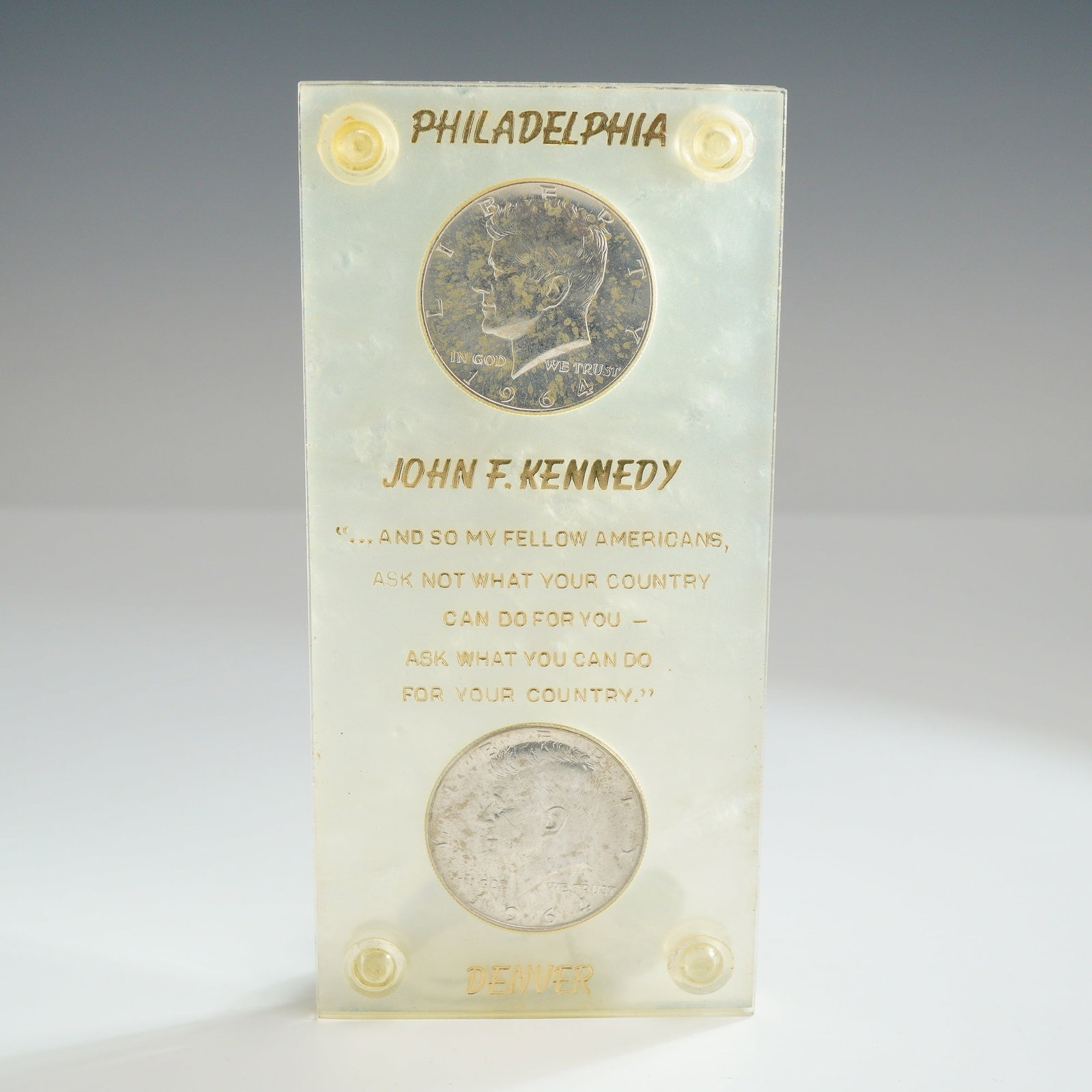 A Pair of US 1964 Kennedy Silver Half Dollars in Memorial Display Case: This numismatic lot consists of a pair of US 1964 Kennedy silver half dollars housed in a commemorative In Memoriam acrylic screw-down holder. The set includes one coin struck at the Philadelphia