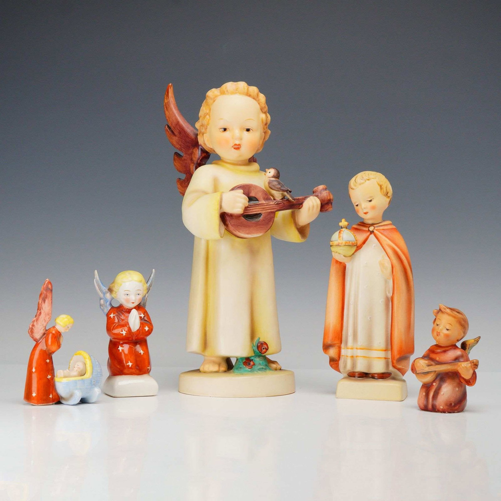 Lot of 5 Germany Marked Hummel and Goebel Porcelain Angel Figurines: A collection of five hand-painted porcelain figurines manufactured by Goebel in Germany, featuring angelic and religious subjects in the M.I. Hummel style. The group is characterized by a soft matte f
