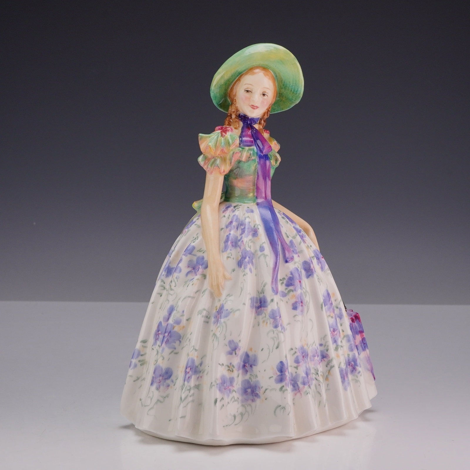 Royal Doulton Bone China Figurine, Easter Day HN1976: Designed by Leslie Harradine, this hand-decorated Royal Doulton figure portrays a graceful woman dressed in a lilac patterned gown accented by a green bodice, elegantly posed holding a parasol. Royal 