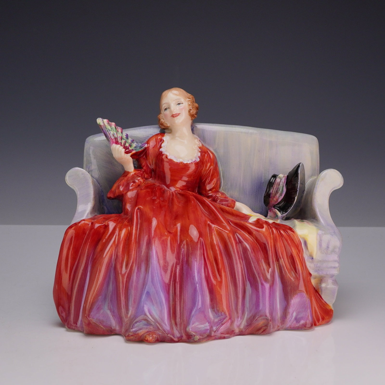 Royal Doulton Bone China Figurine, Sweet & Twenty HN1298: Designed by Leslie Harradine, this elegant Royal Doulton figure portrays a woman seated gracefully upon a couch, dressed in a flowing red gown. The figure's title is inspired by the song "Oh Mistress 